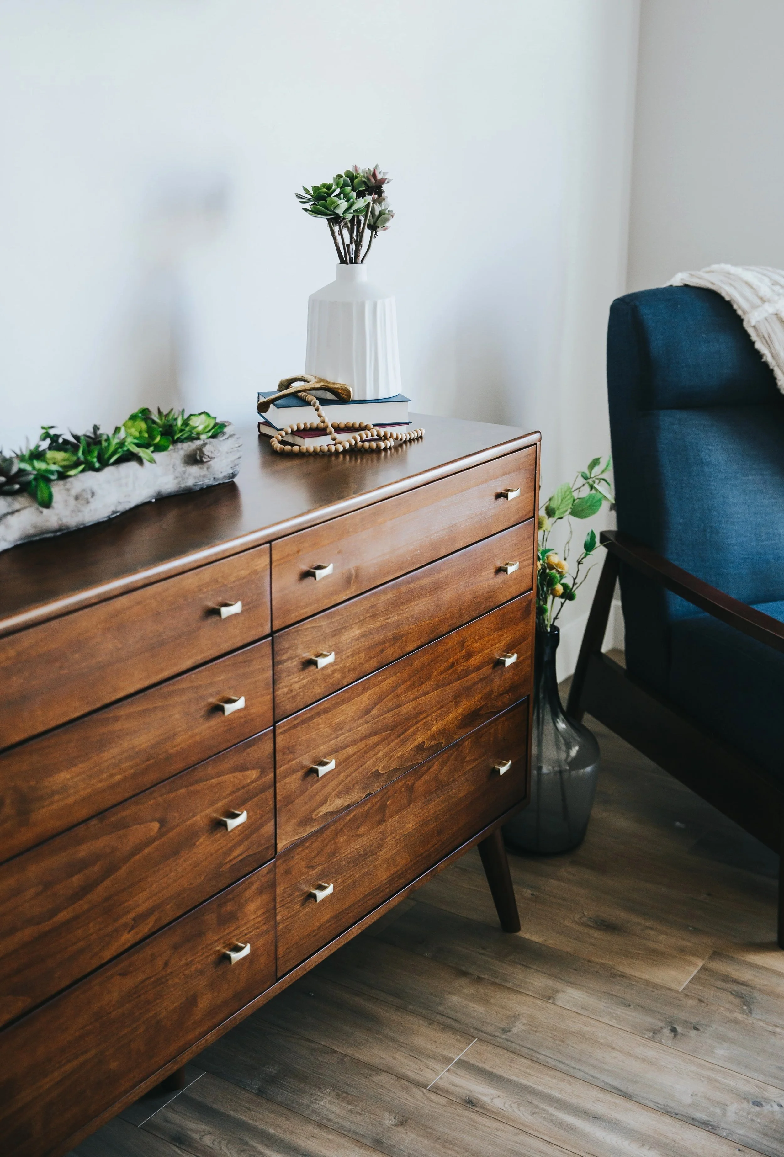 Wooden mid-century dresser decorated with potted succulents and books indoors.
