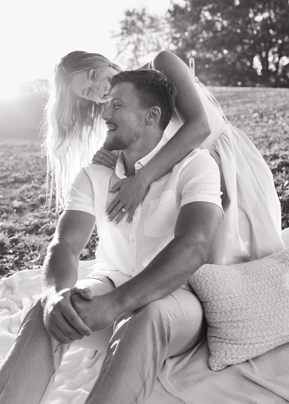 A black and white photo of a newly engaged couple laughing together at a picnic
