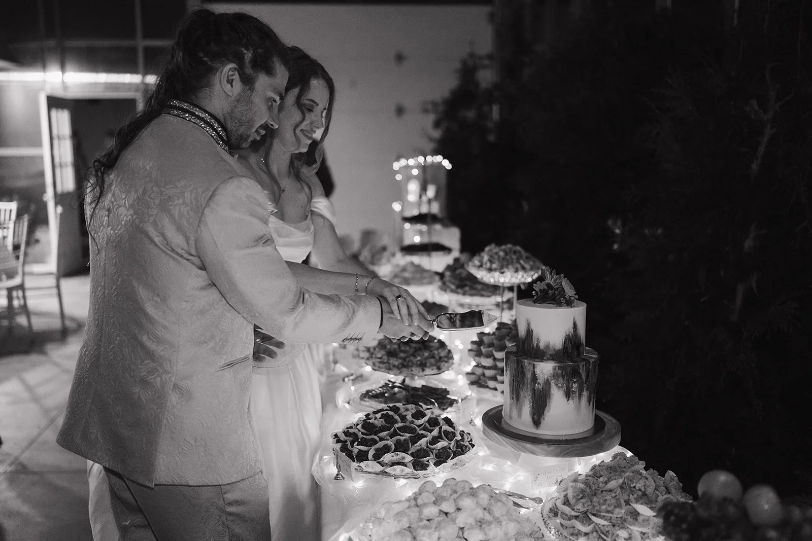 Black and white photo of a bride and groom cutting into their wedding cake.