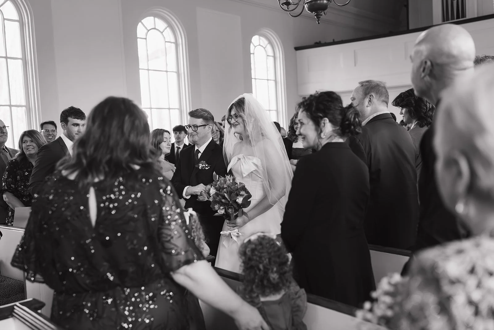 Black and white photo of a bride being walked down the aisle by her father for her Martha-Mary Chapel wedding ceremony.