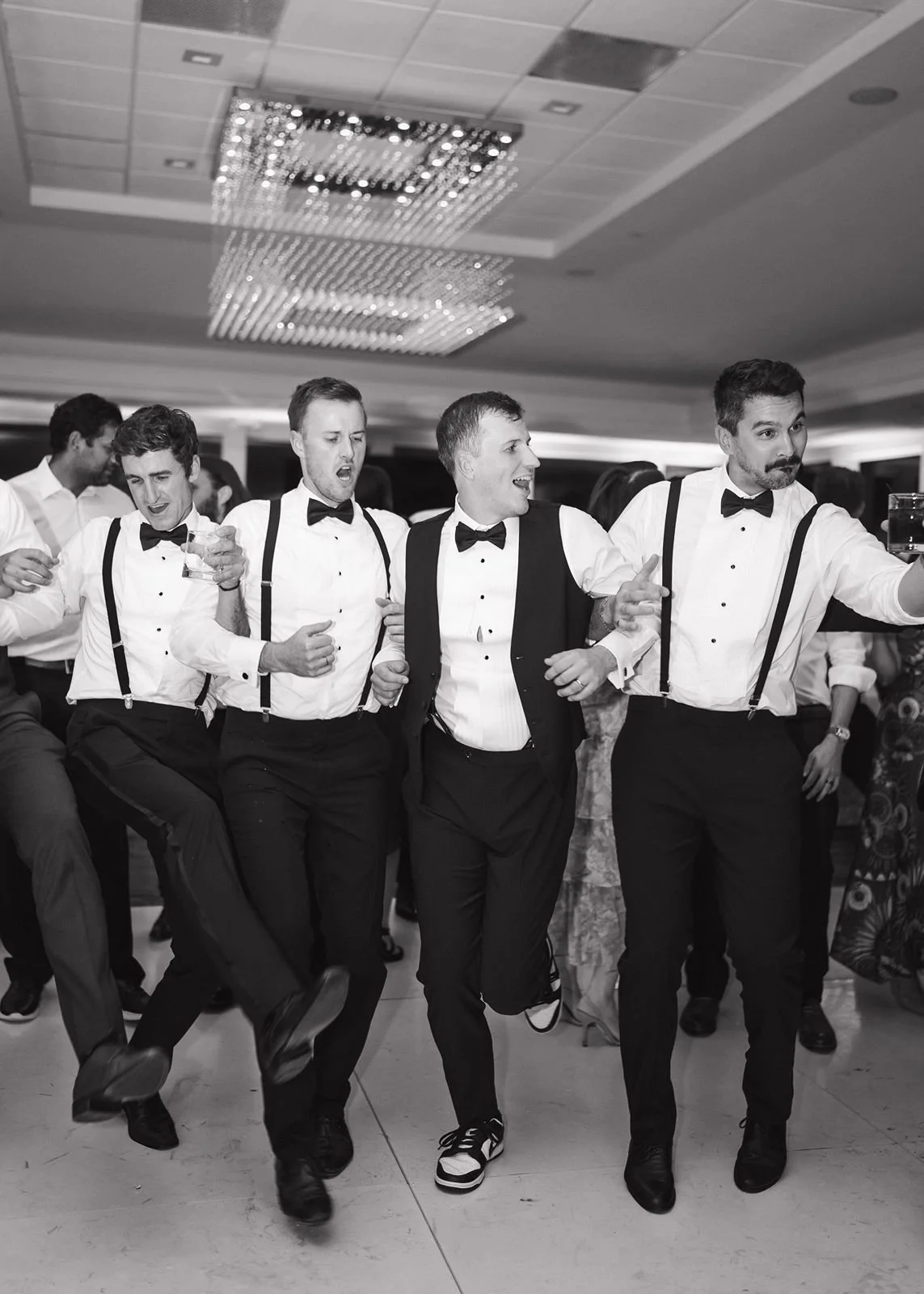 A black and white photo of a groom doing a line dance with his groomsmen.