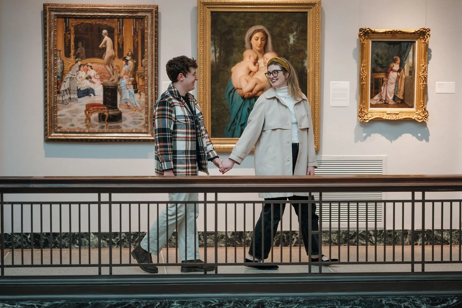 Engaged couple walking together inside University of Michigan Museum of Art with ornate gold framed gallery walls and classical architecture