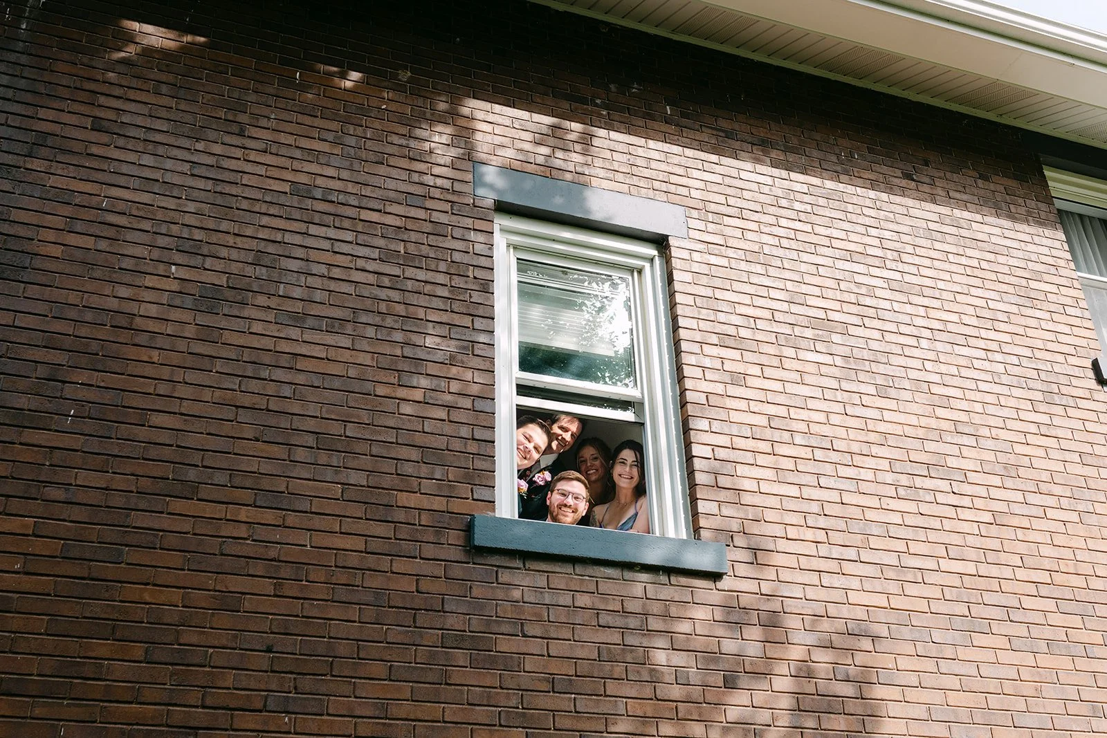 Brides friends peeking out the second story window at Brownstone Haus in Frankenmuth during the first look.