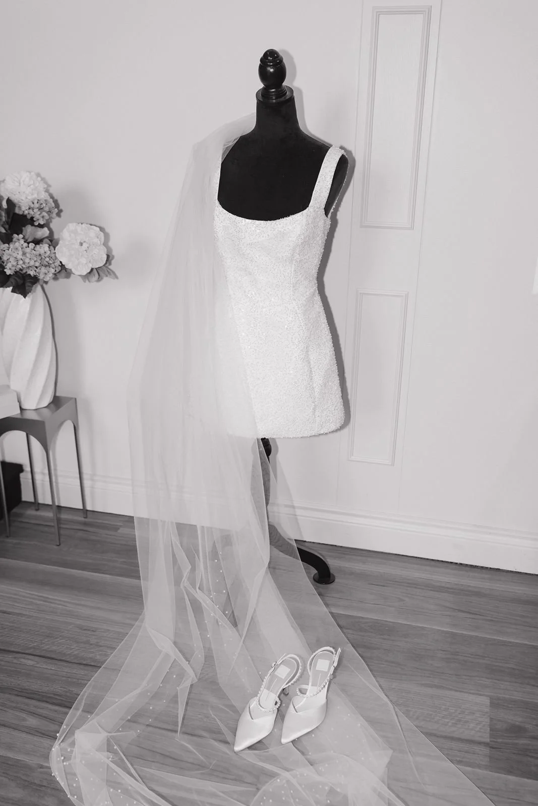 A short white dress with a veil draped over the shoulder on a mannequin.