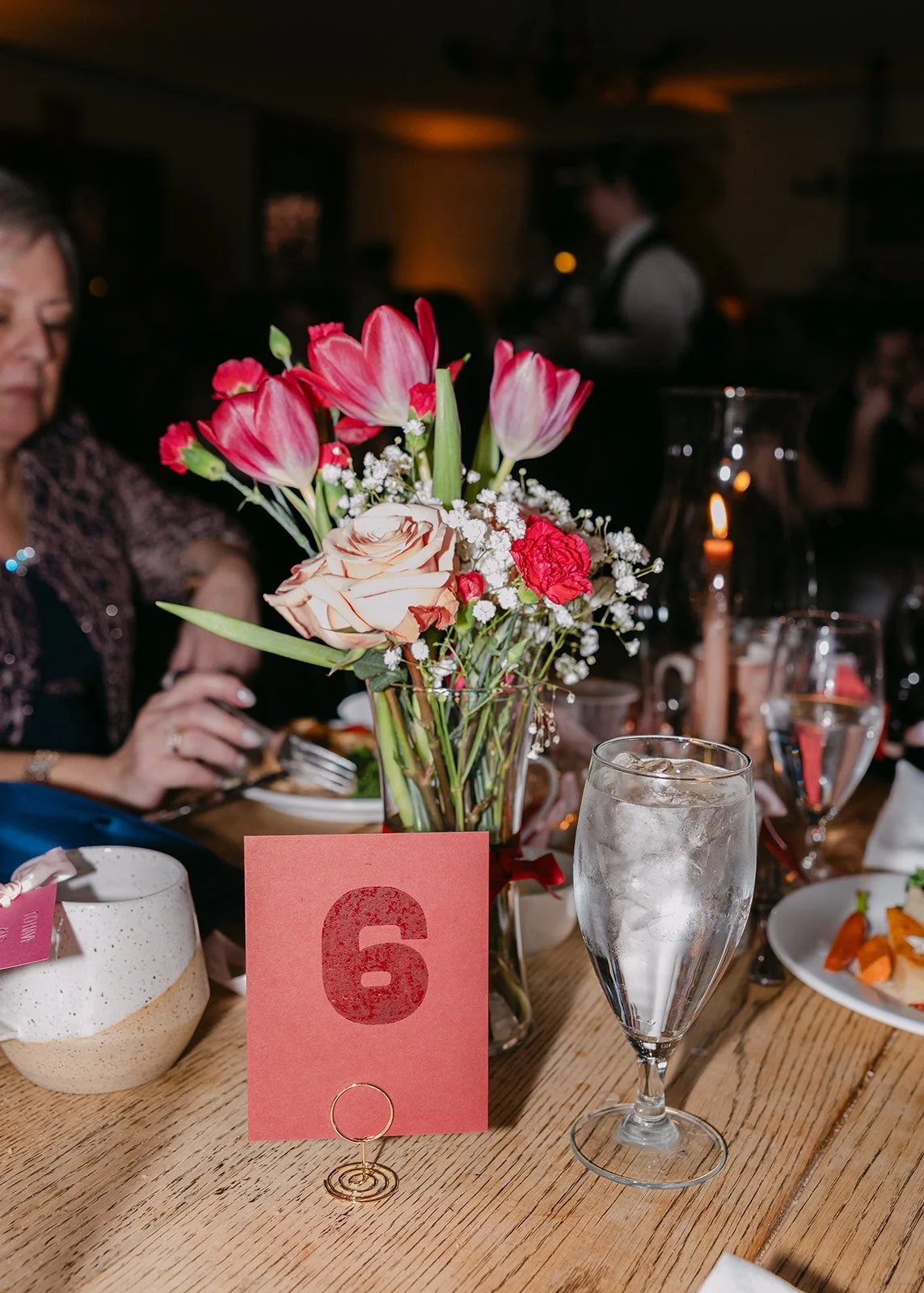 Wedding reception table setting with florals, drinks, table numbers, and guests eating at Eagle Tavern at Greenfield Village.