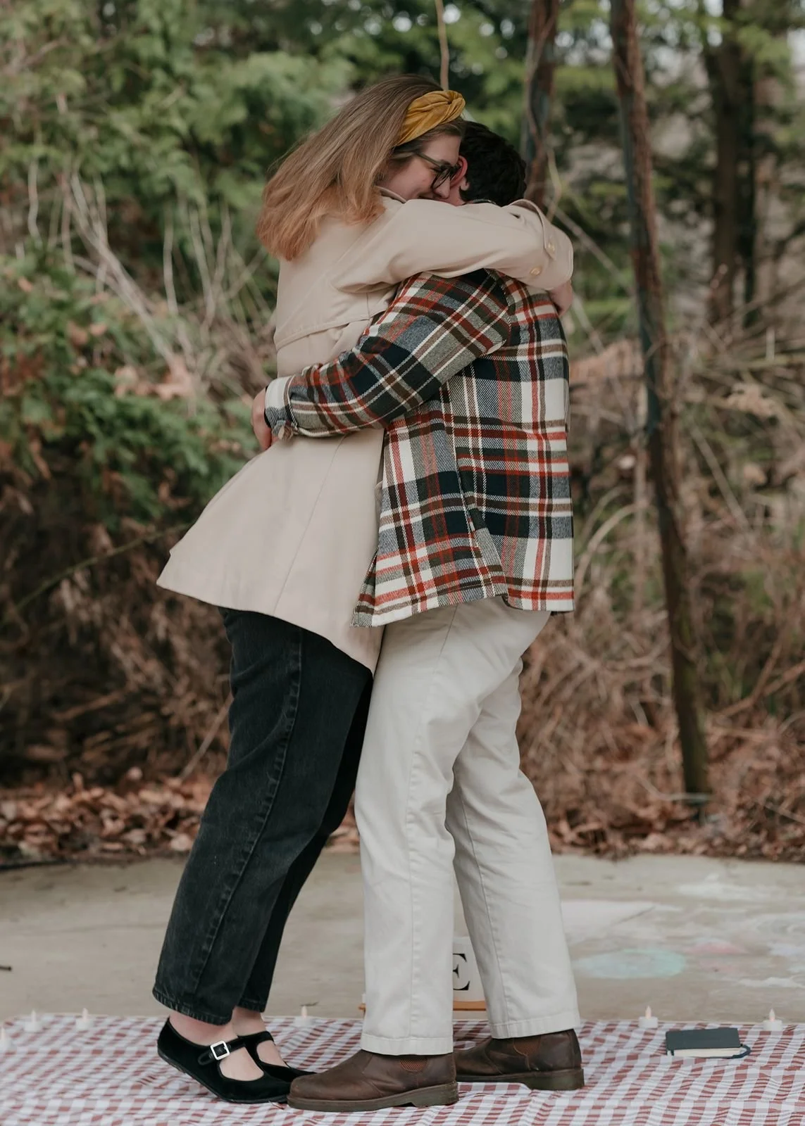 Engaged couple embracing on picnic blanket during outdoor proposal at Nichols Arboretum Ann Arbor, Michigan with cozy fall styling