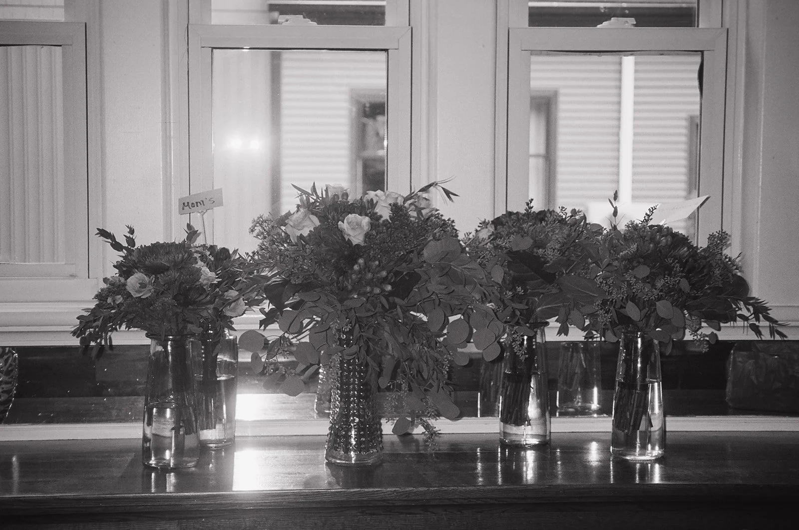 Black and white film photo of bouquets sitting in vases prior to the wedding.