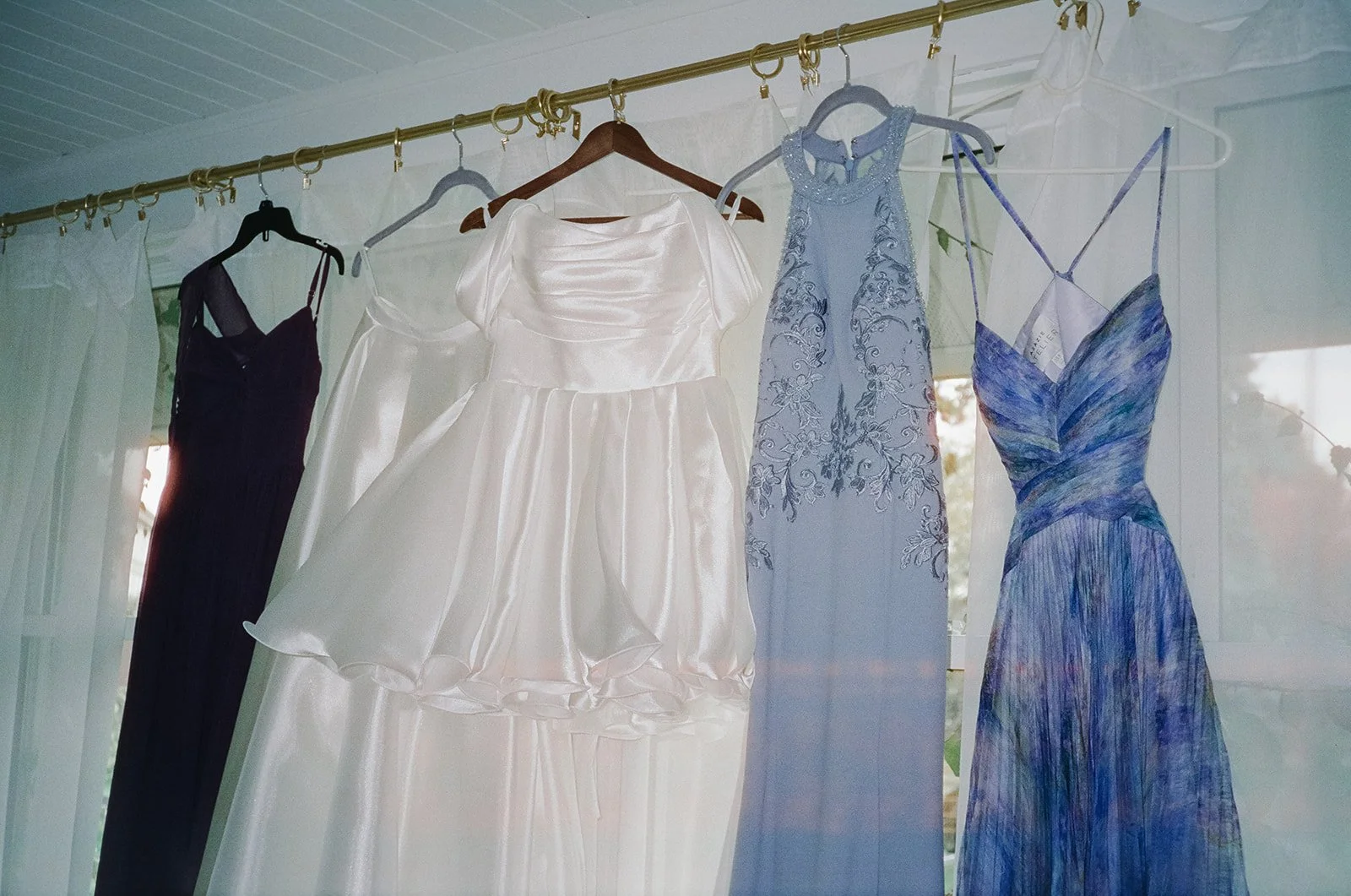 Film photo of the brides dresses as well as bridesmaids dresses hanging in front of a window.