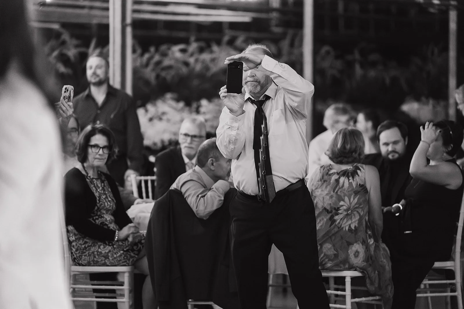 Black and white photo of a guest taking a photo of the groom dancing with his mother.