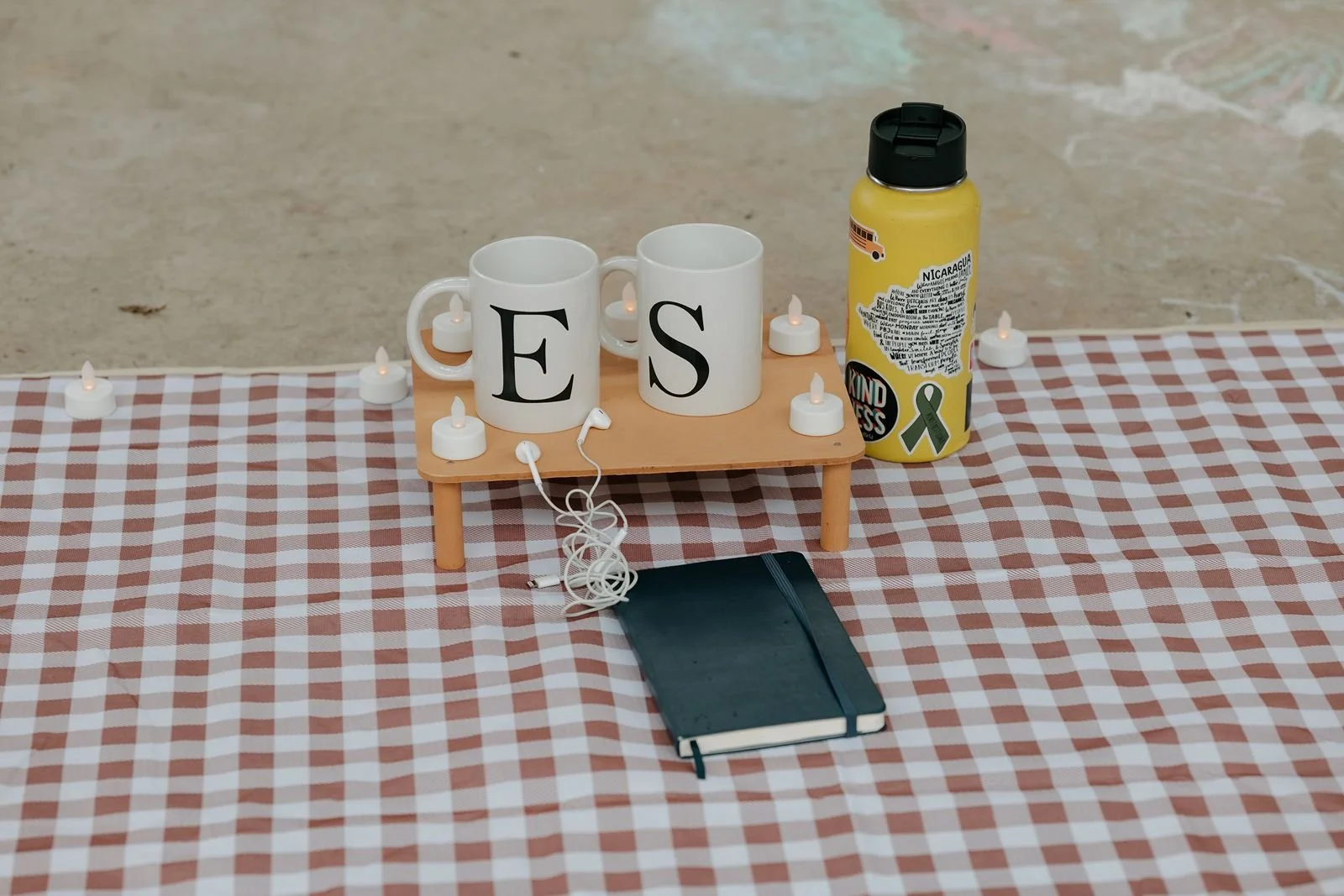 Flat lay of proposal picnic setup with initial mugs, candles, notebook, and personal details for Ann Arbor engagement