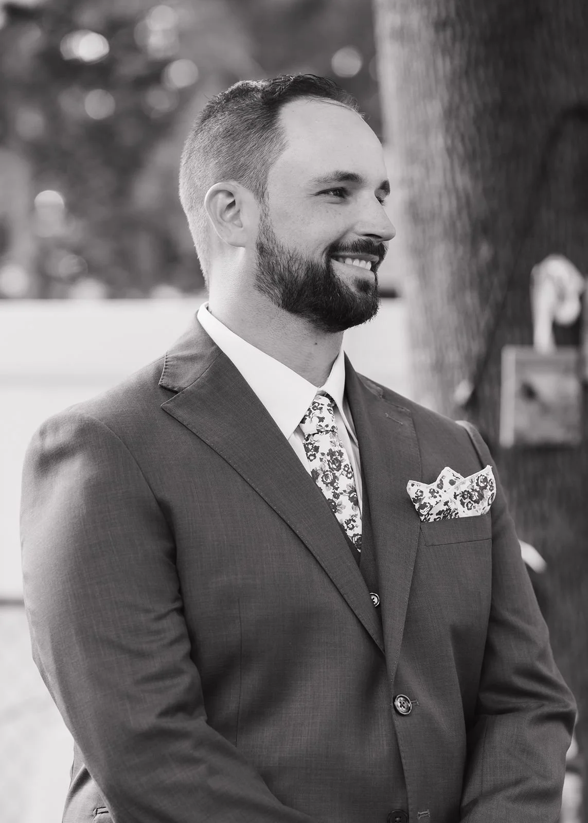 A black and white photo of a groom seeing his bride walking down the aisle for the first time. He has a huge smile on his face. They are getting married in the backyard of a family property.