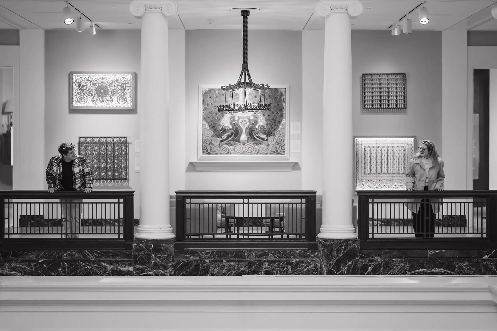 Black and white photo of couple across museum balcony at UMMA in Ann Arbor, creating a cinematic and architectural composition