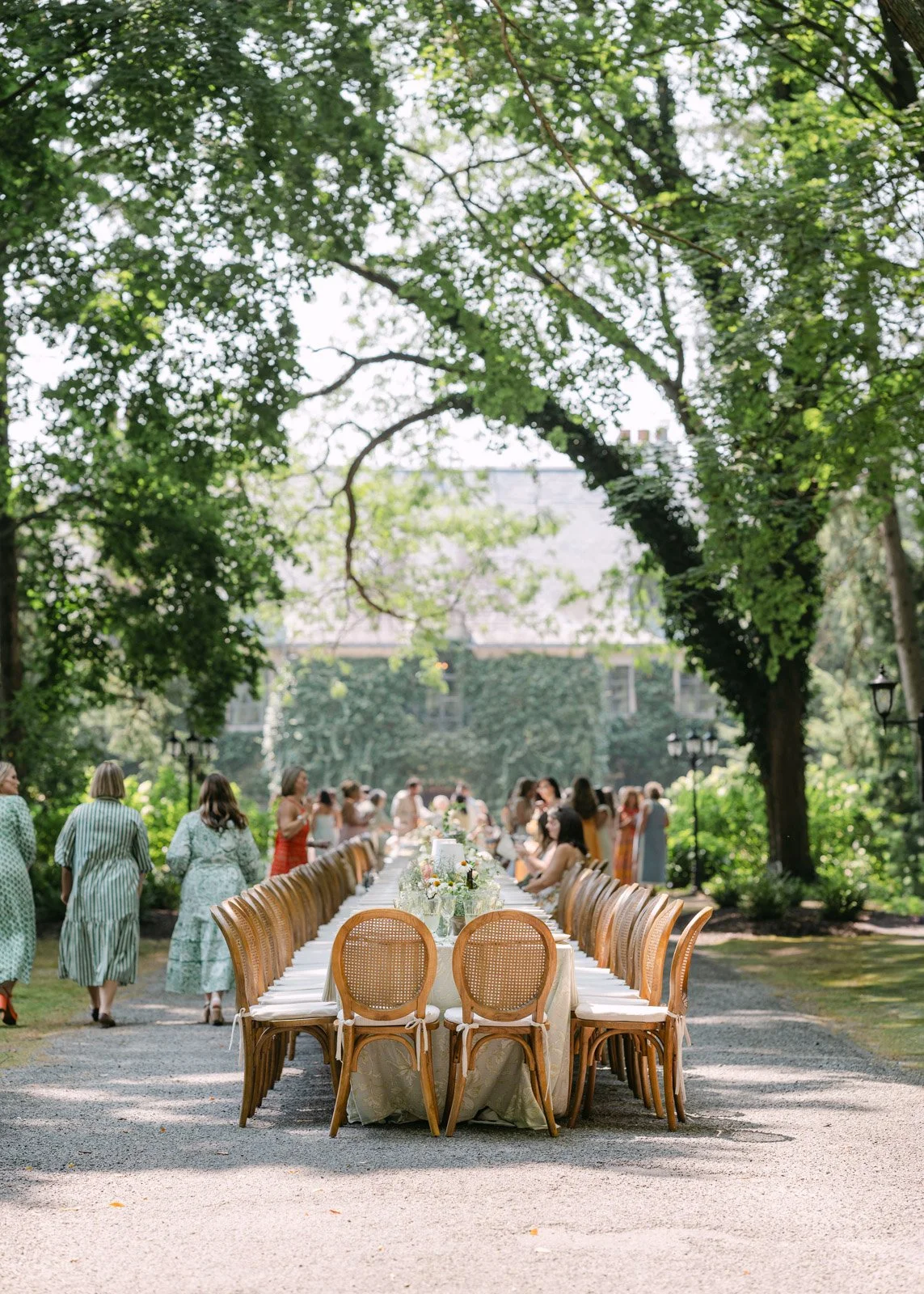 A long wedding table with cane back wedding chairs, placed along the driveway up to Greencrest Manor.