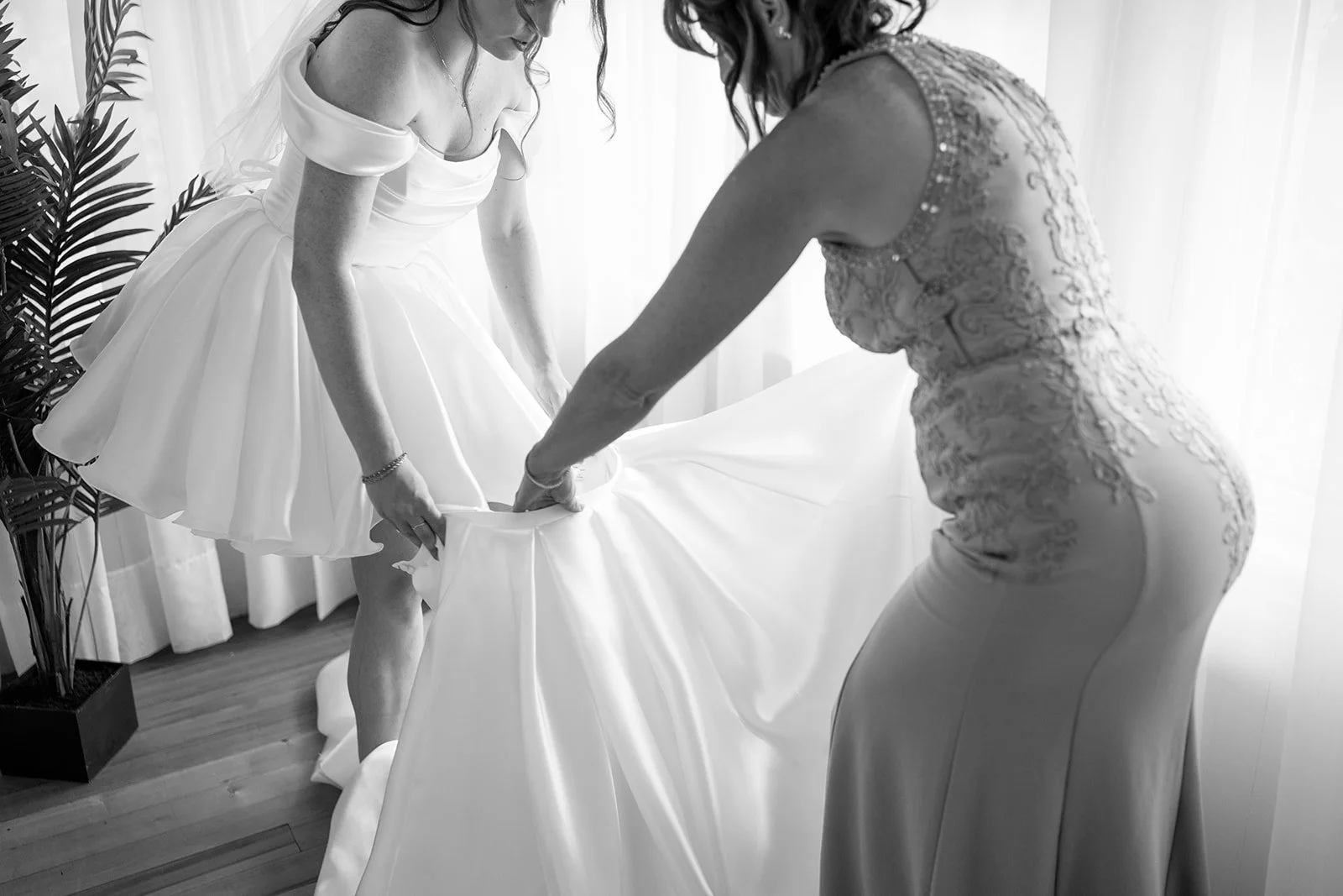 Black and white photo of the brides mother helping her into her dress,