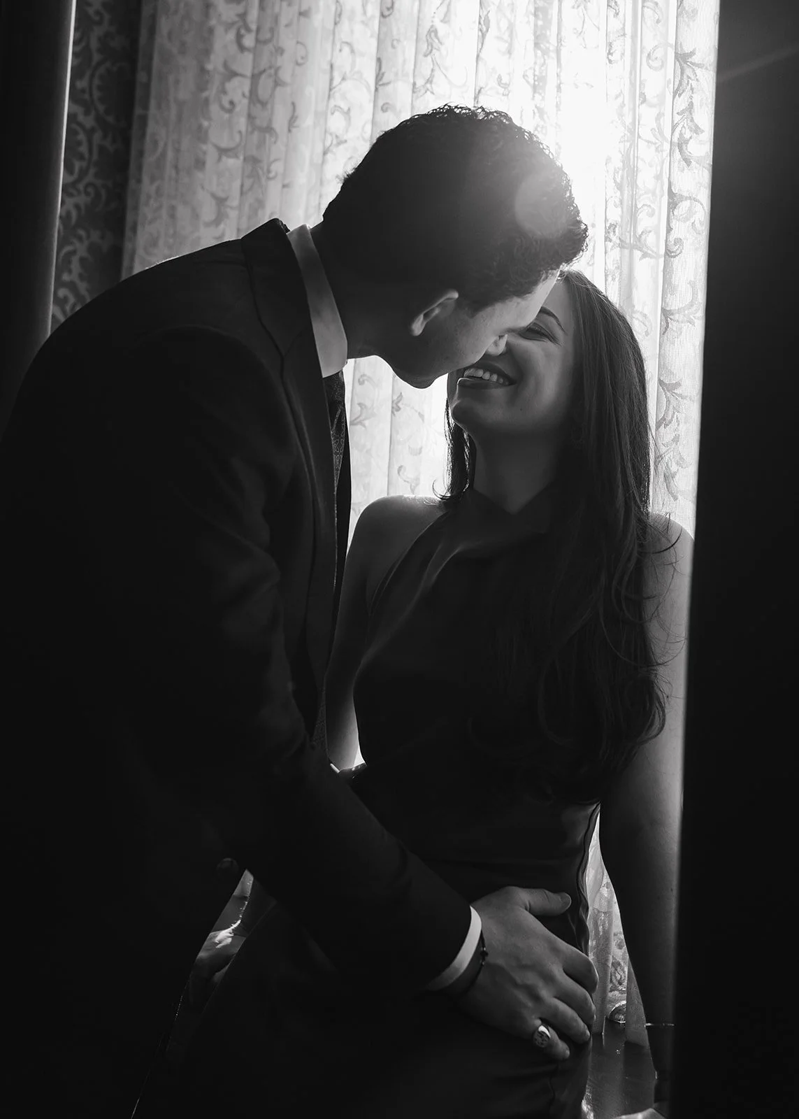 Black and white photo of a man leaning in for a kiss from his fiancé.