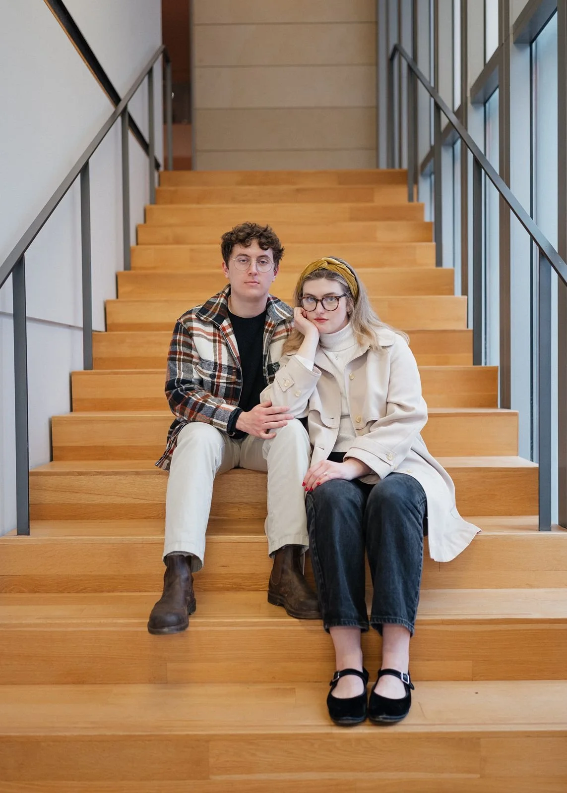 Engaged couple sitting on modern wooden staircase at University of Michigan Museum of Art smiling during engagement session