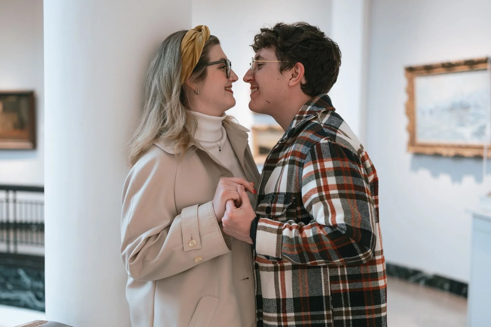 Engaged couple holding hands and smiling at each other inside art museum gallery during Ann Arbor engagement session