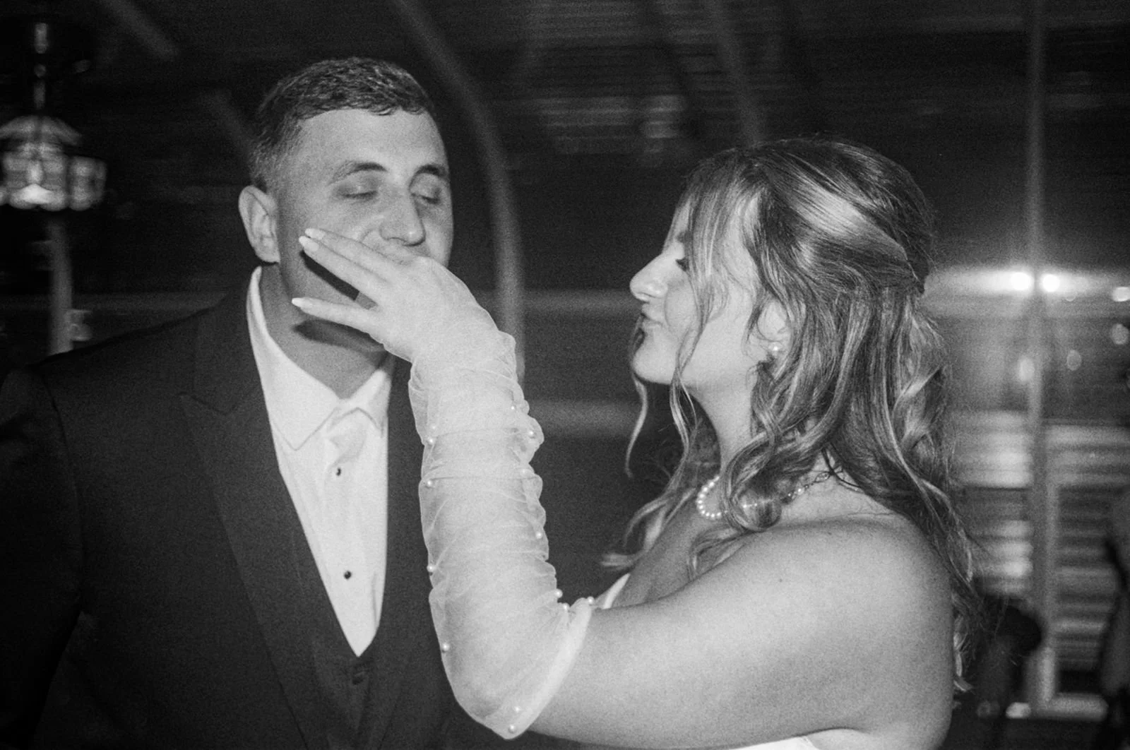 A black and white film photo of a newly married couple cutting their wedding cake and feeding it to each other.