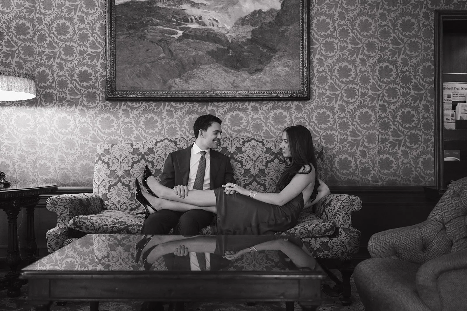 Black and white wide shot of a couple sitting on a couch inside The Detroit Athletic Club for their engagement session.