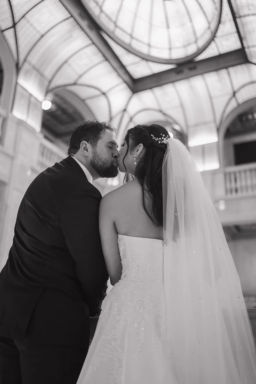 Black and white photo of a bride and groom kissing on the second floor of Book Tower.