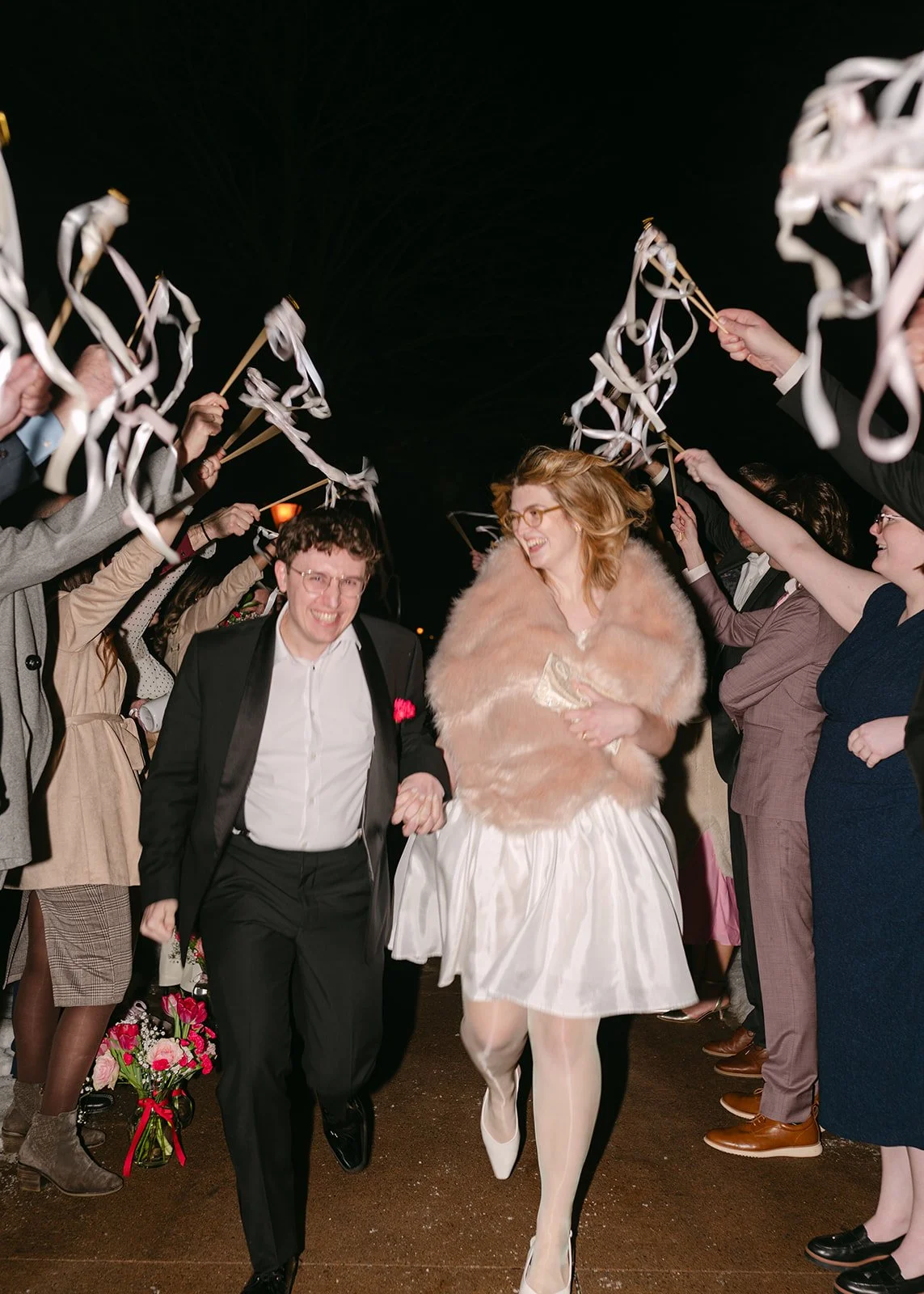 Bride and groom running through a tunnel of guests during their wedding reception exit at night.