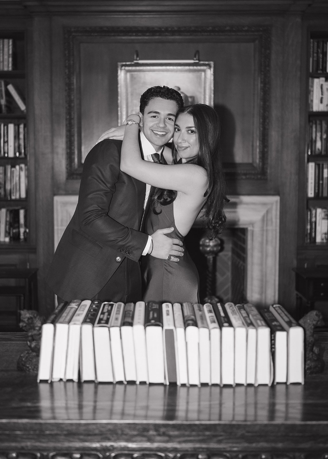 Black and white photo of a couple hugging in front of a desk with books for t heir elegant Detroit Athletic Club engagement photos.