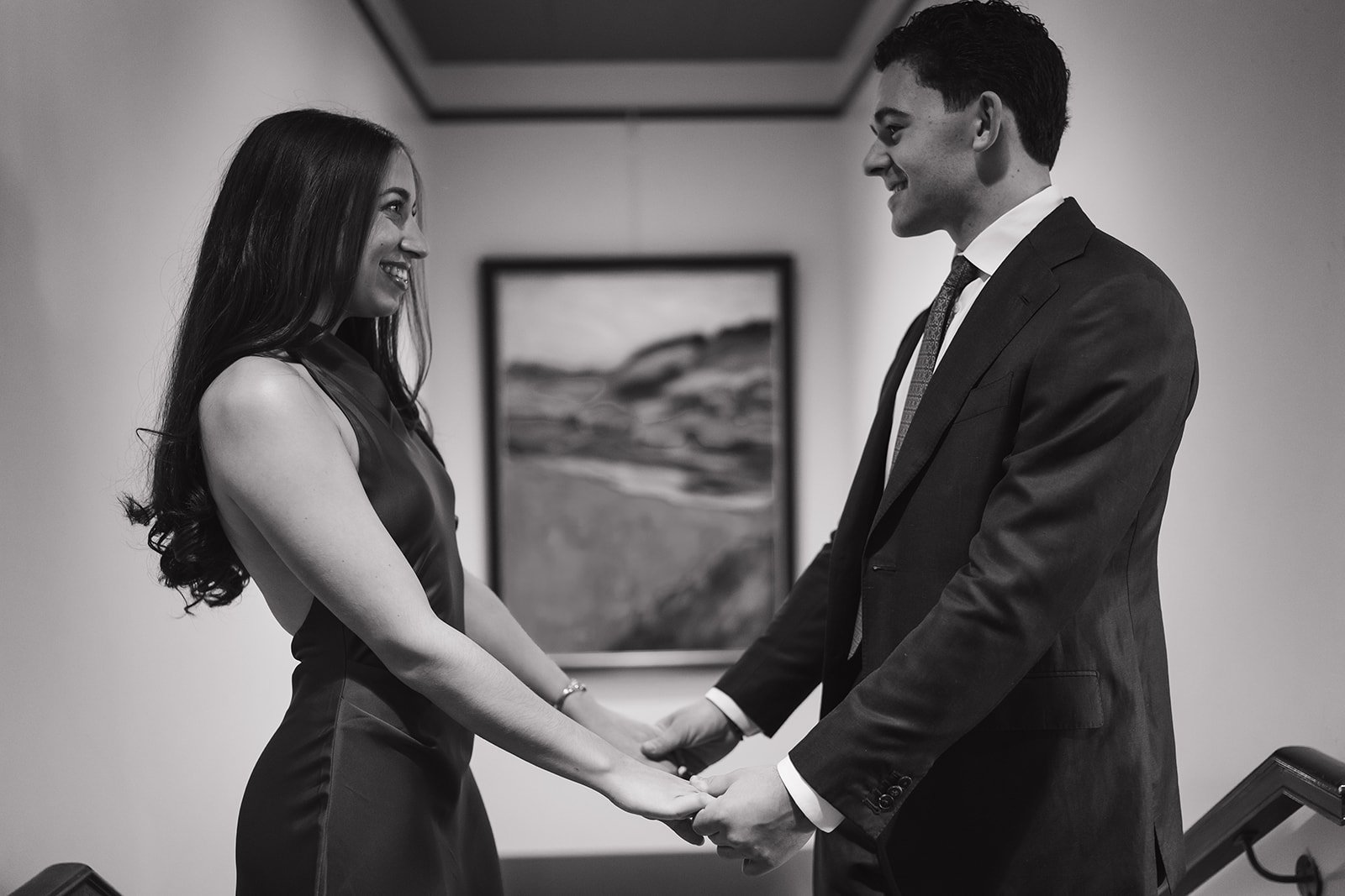 Black and white wide shot of a couple holding hands in front of one another during their Detroit engagement photos at the DAC.