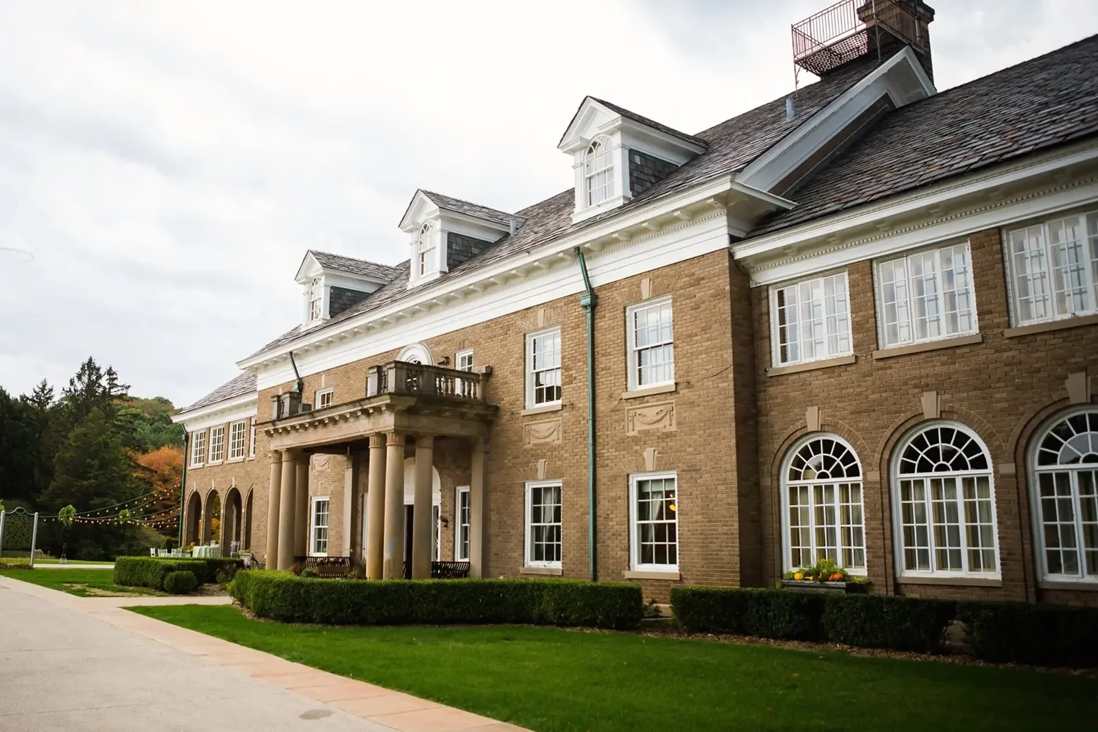 A photo of The Felt Estate wedding venue in Holland, Michigan featuring light colored brick, a dark grey roof, arched windows and an awning over the entryway.
