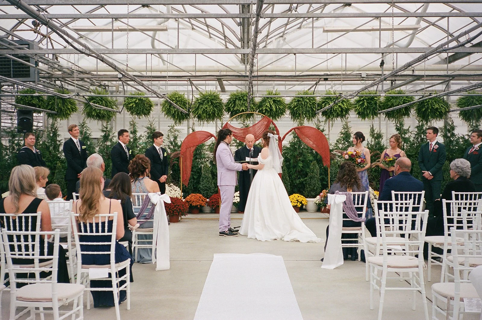 Film photo of a bride and groom holding hands at the altar during their Abele Greenhouse wedding ceremony in Saginaw, Michigan.