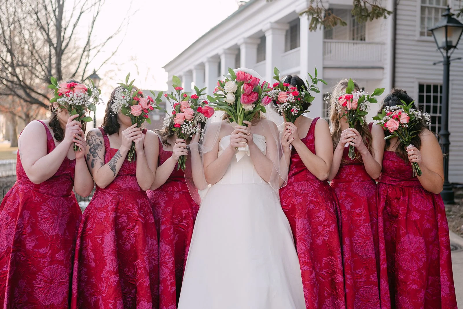 Outdoor bride and bridesmaid photo with them holding up bouquets over their faces for portraits.