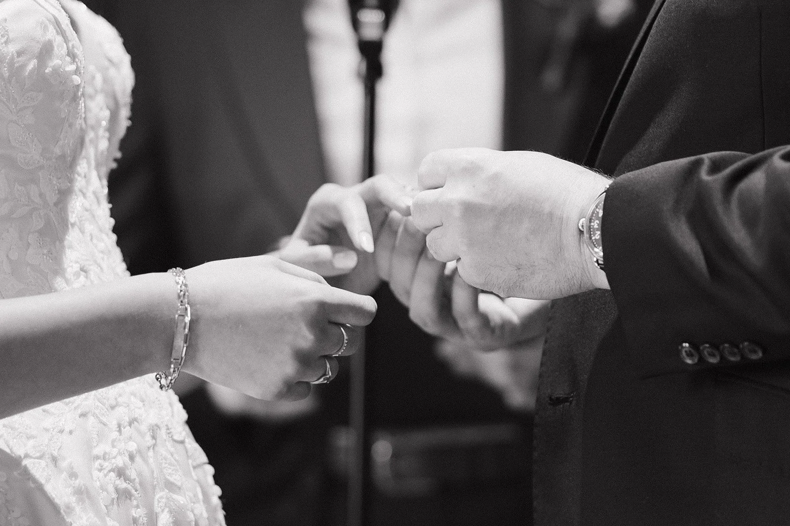 Black and white photo of a bride and groom exchanging rings during the ceremony.