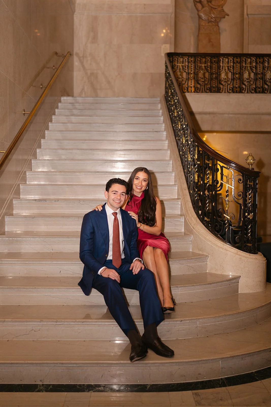 Couple smiling at the camera while sitting on a white satiarcvaser at the Detroit Athletic Club for their engagement photos.