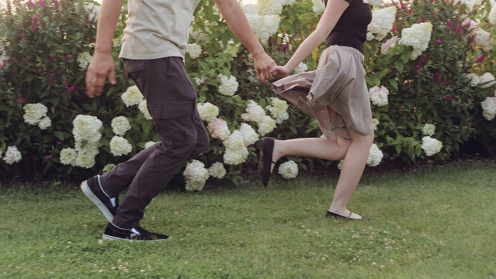 Close up photo of a couple running whole holding hanfs in front of flower bushes for their Detroit engagement photos.