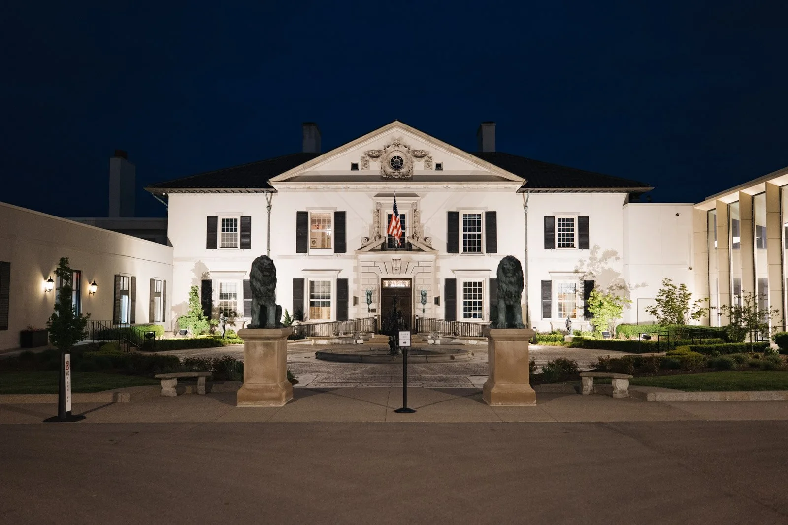 An exterior of the front of The War Memorial venue in Grosse Pointe Farms at night. The venue is lit up by ground lights, leaning into the stately feel of the wedding venue.