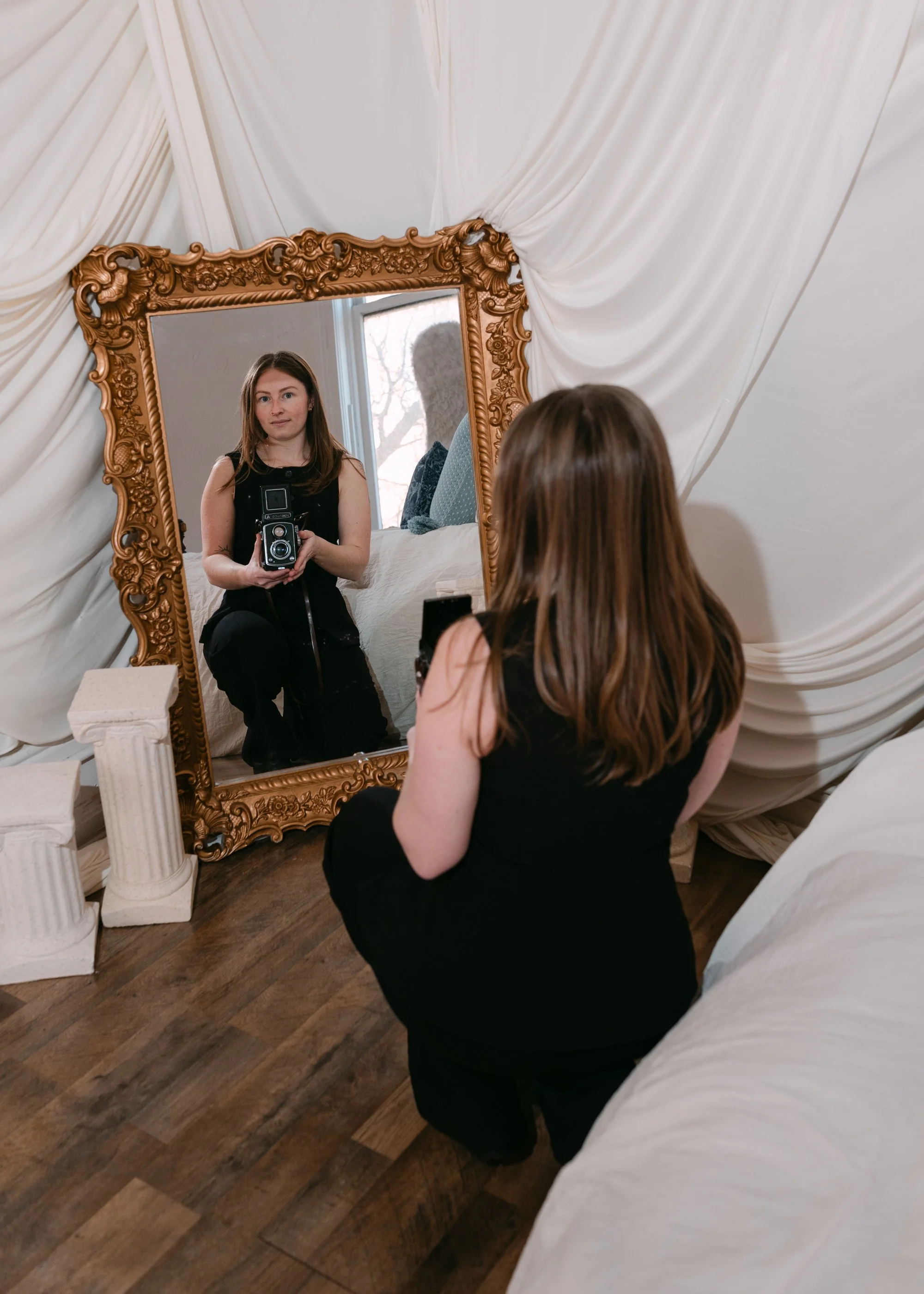 Alaina of Alaina Miller Photography posing with a camera through a vintage mirror.