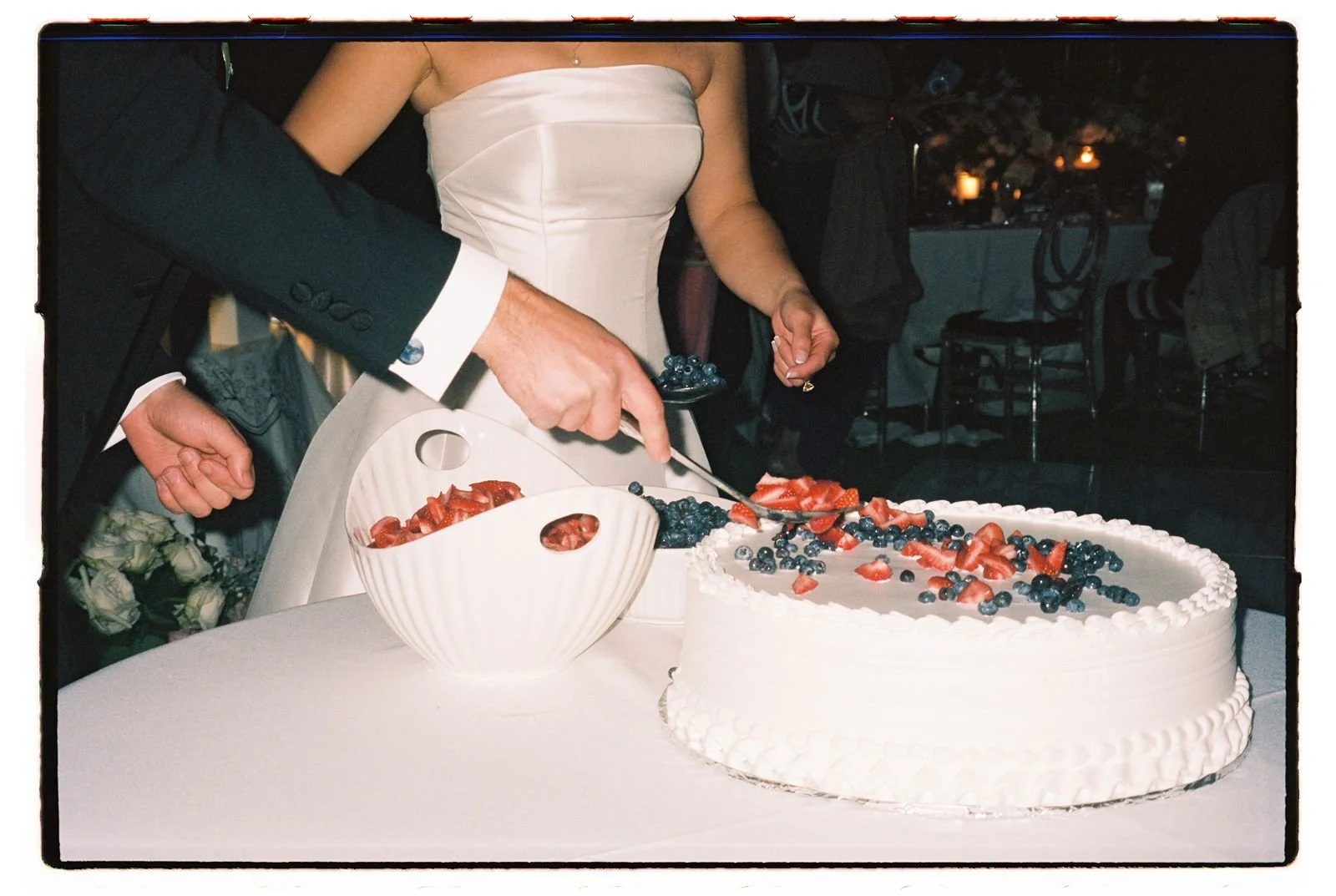 A 35mm close up photo of a bride and groom cutting their 1-tier cake with berries on top.