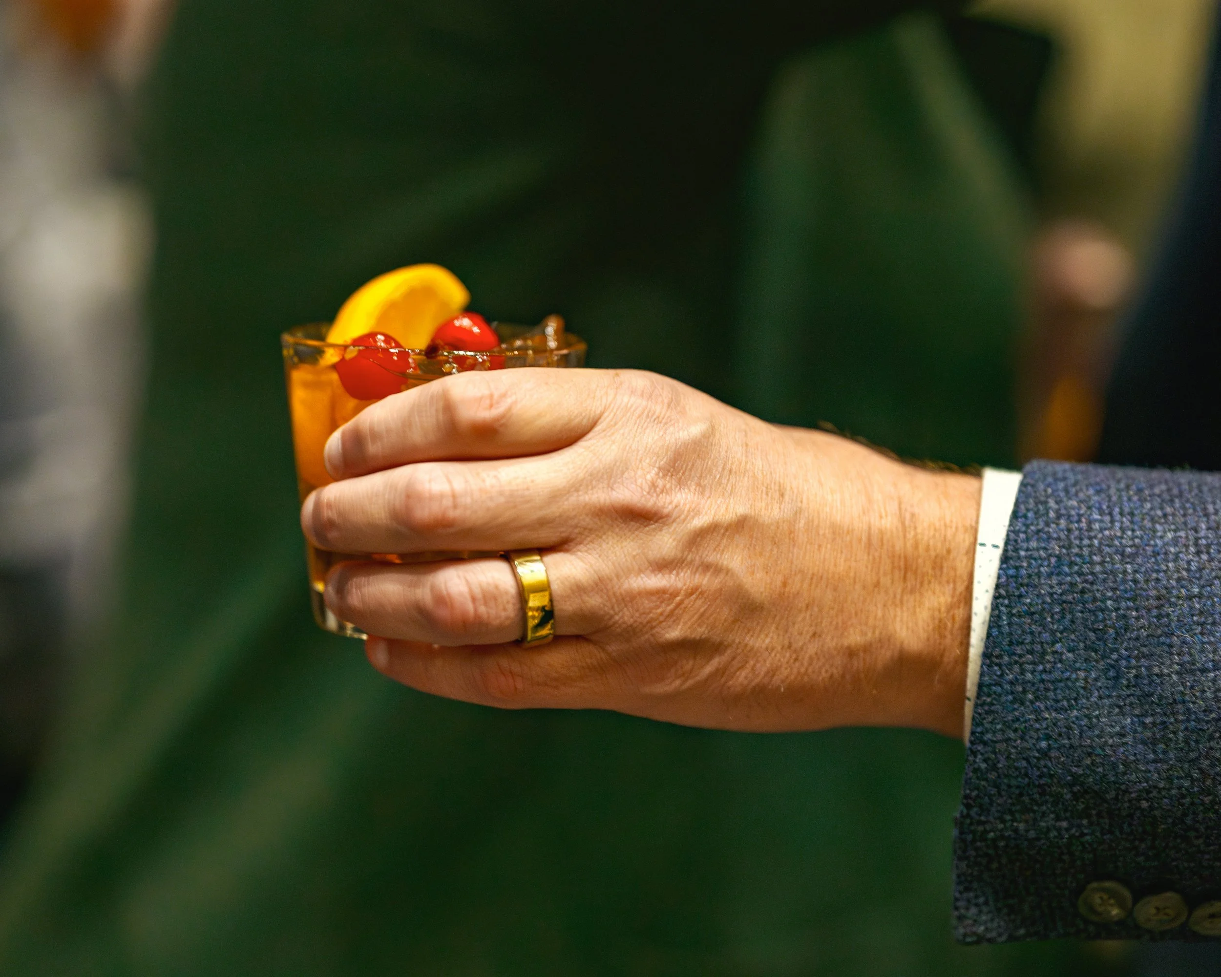 A close up of a married man's hand holding an old-fashioned cocktail.