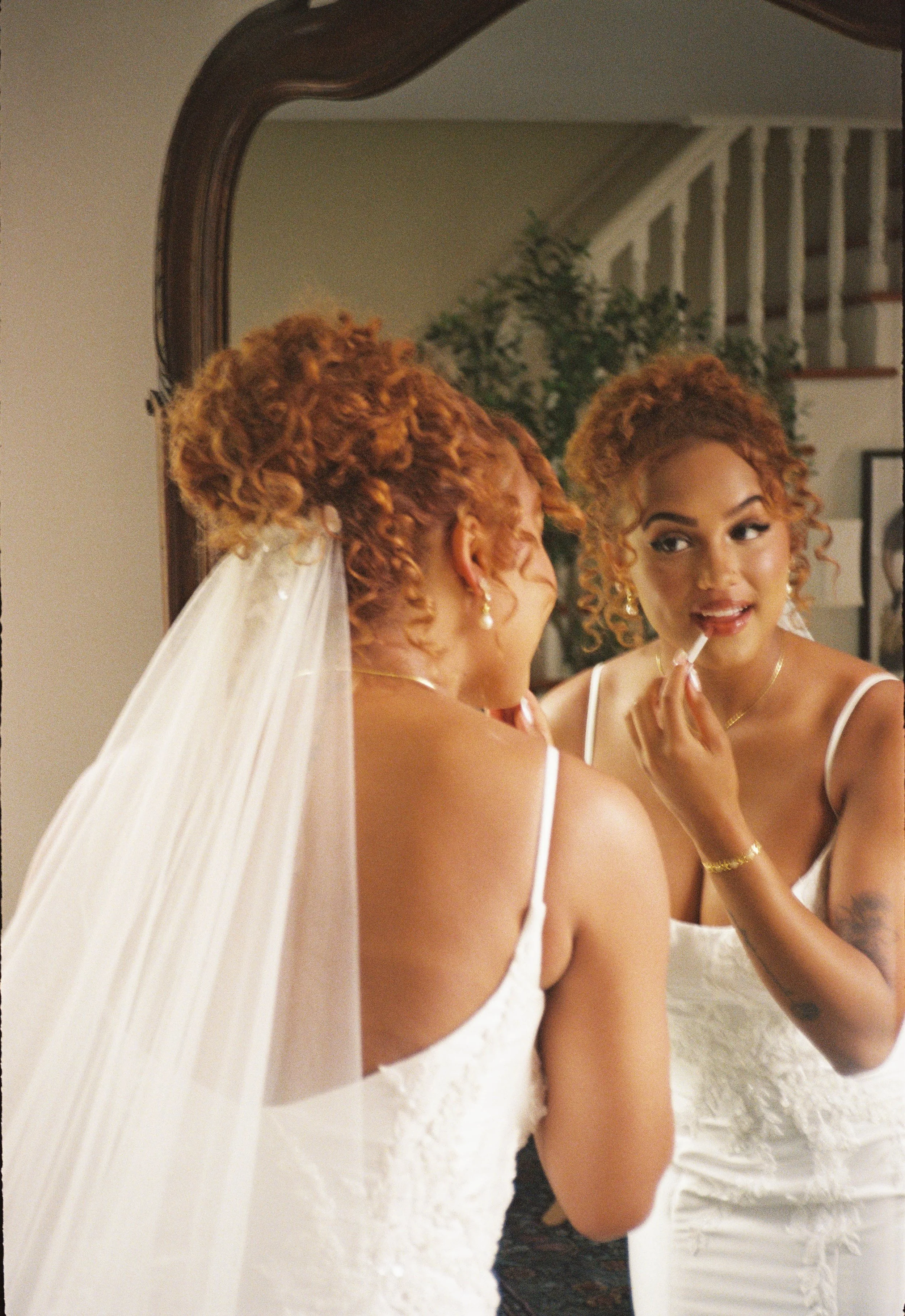 A 35mm photo of a bride with a curly updo, as she re-applies her lipstick in the mirror.