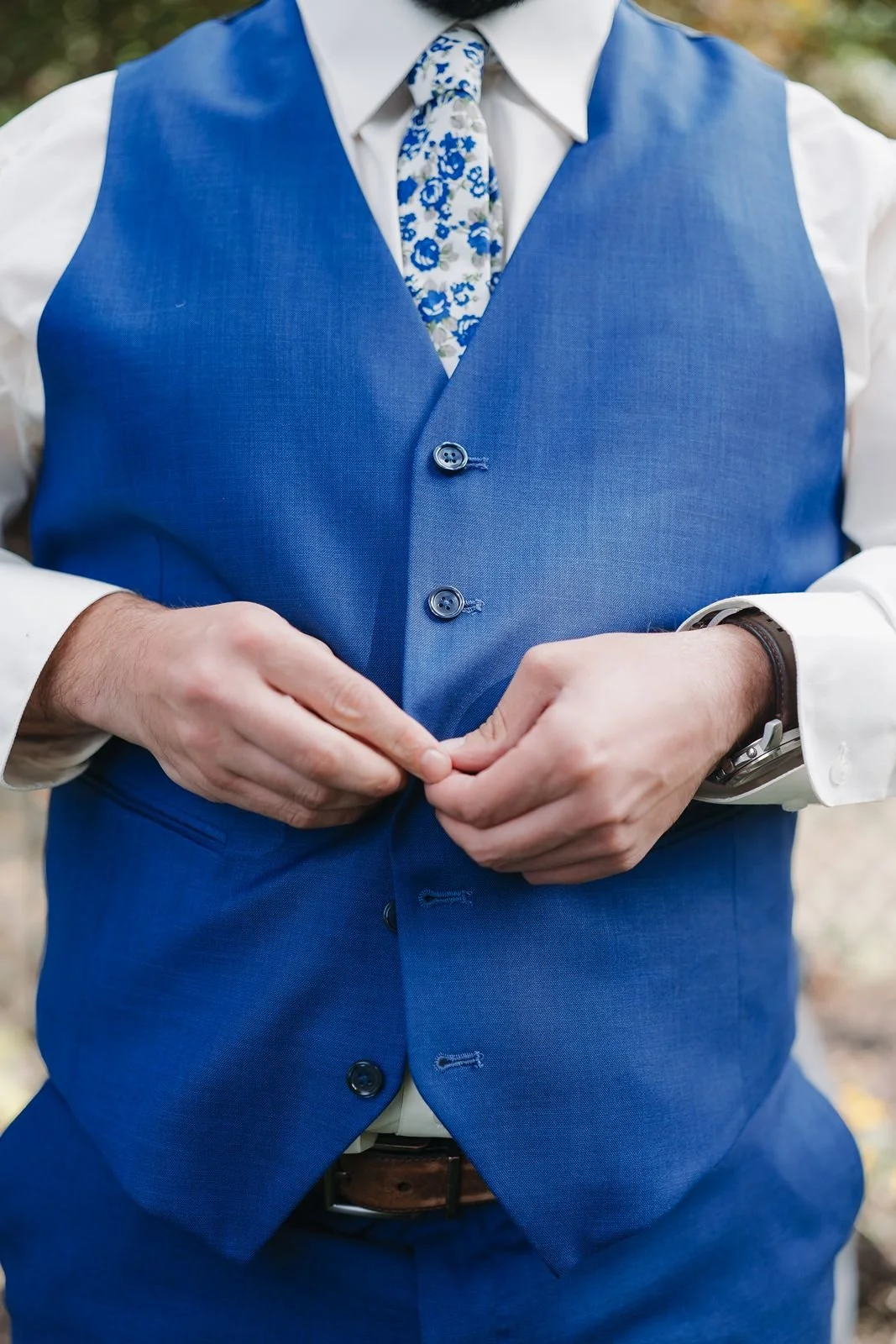 A groom buttoning his blue vest before his backyard wedding ceremony