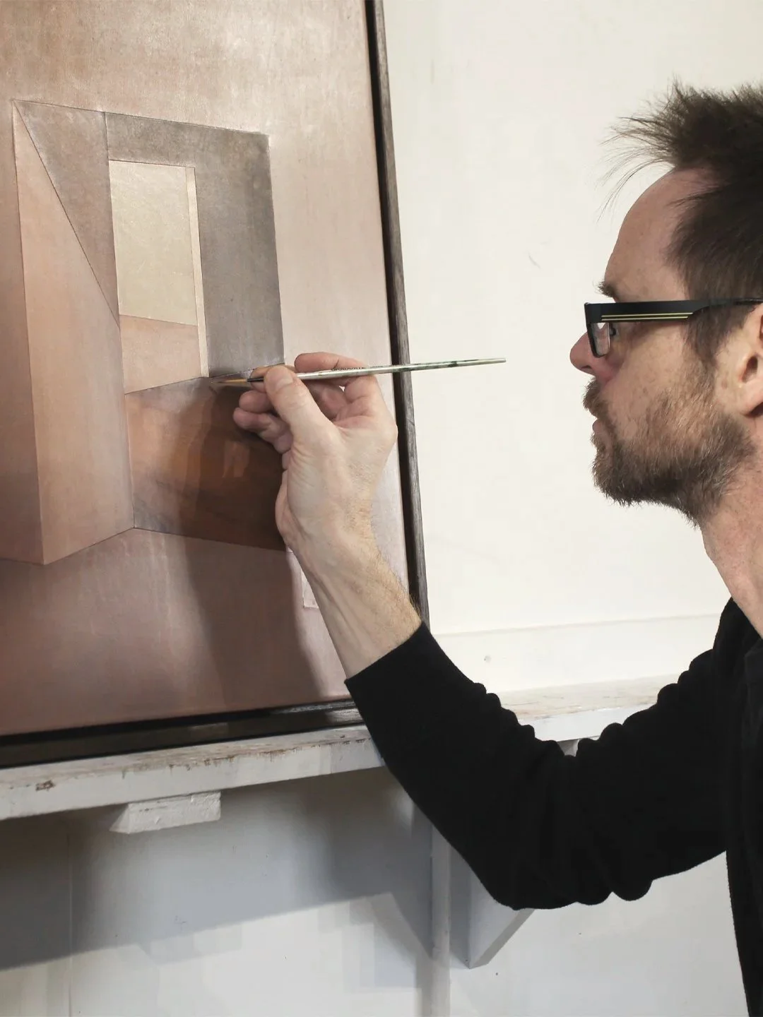 Neale Marriott in his studio painting a geometric design on a leather marquetry surface with a fine brush inspired by architectural spaces for Marrikur Design Studios.