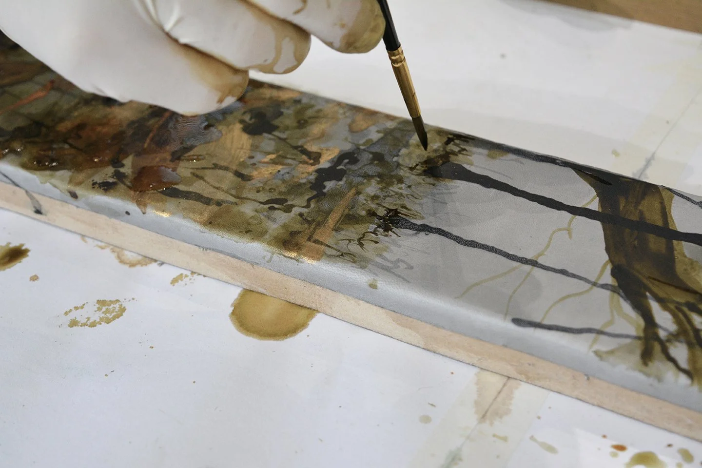 close up of marrikur studios hand painting a neutral leather mirror frame with a woodland scene in trees using natural inks