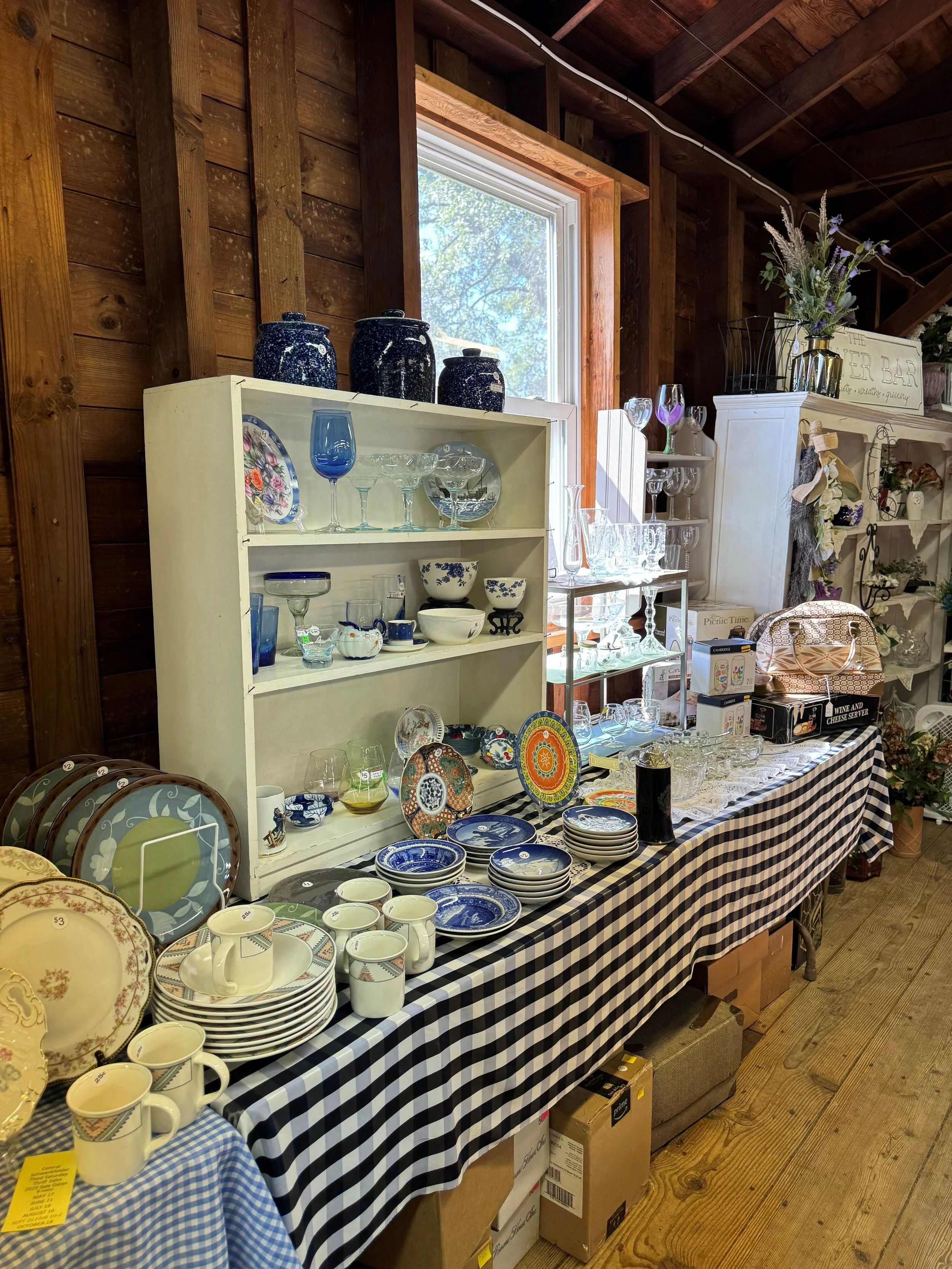 Vintage kitchen decor including jars labeled 'FLOUR' and 'favori', a small copper pot, decorative dolls, and dishware on a wooden shelf with a textured wall in the background.