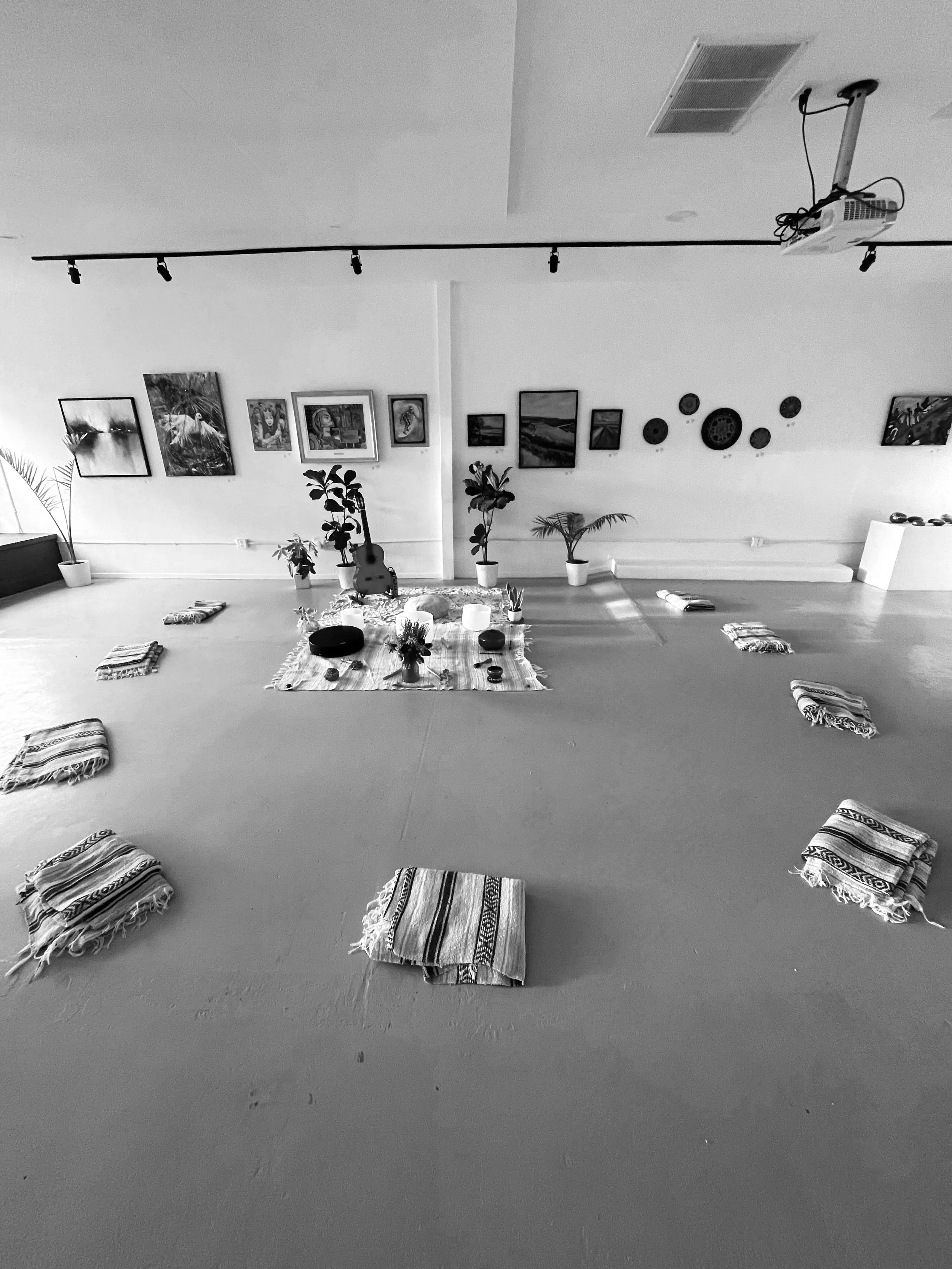 An indoor space set up for a meditation or yoga session with cushions, a central blanket, plants, and artwork on the walls.