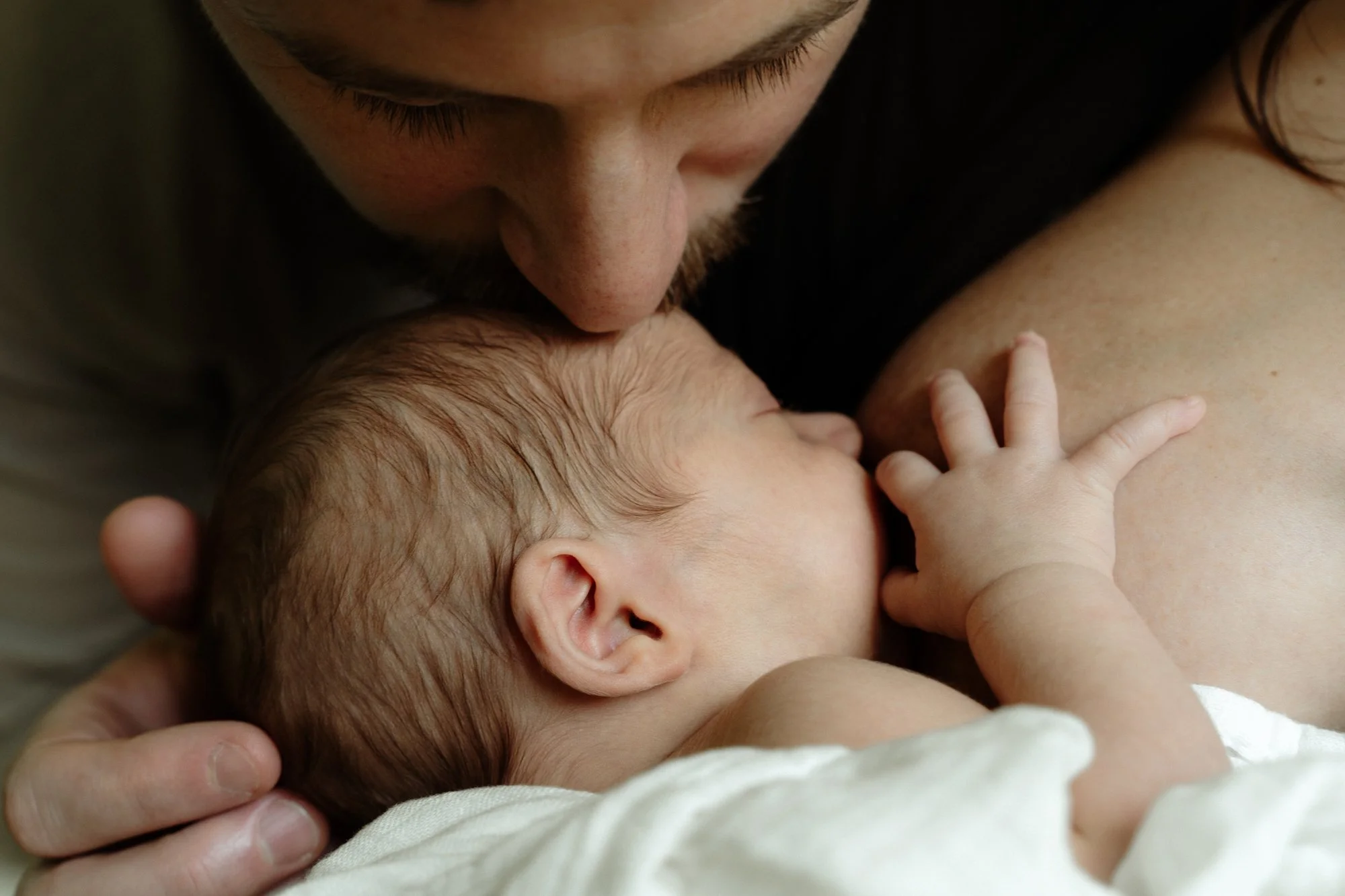 Close-up of a man breastfeeding a newborn baby, with the baby's hand resting on the man's chest.