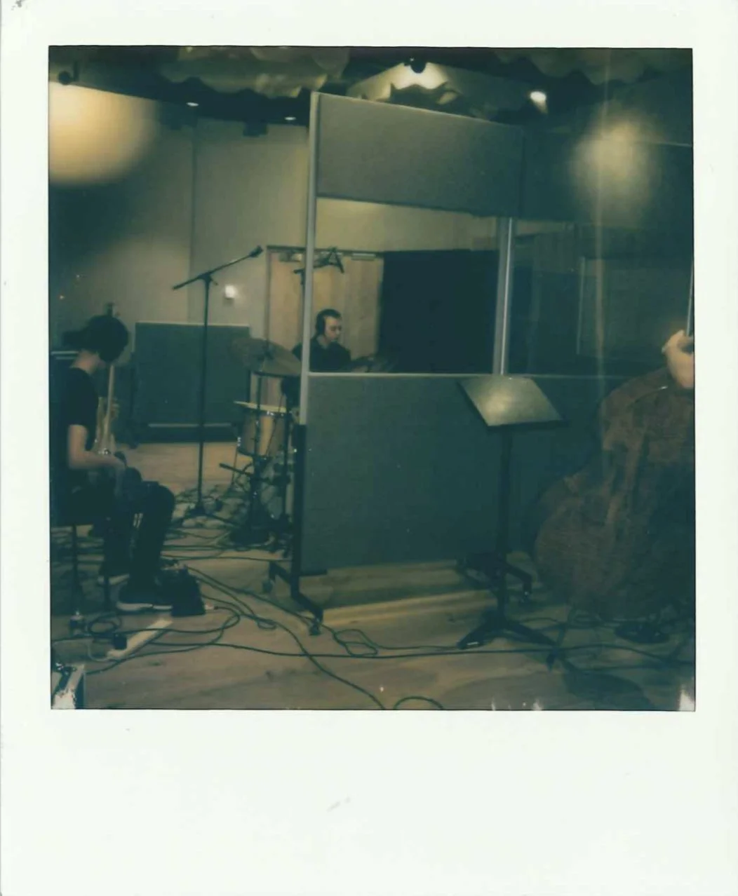 Musicians practicing in a recording studio, with instruments including a saxophone and drums, and a person at a computer monitor.