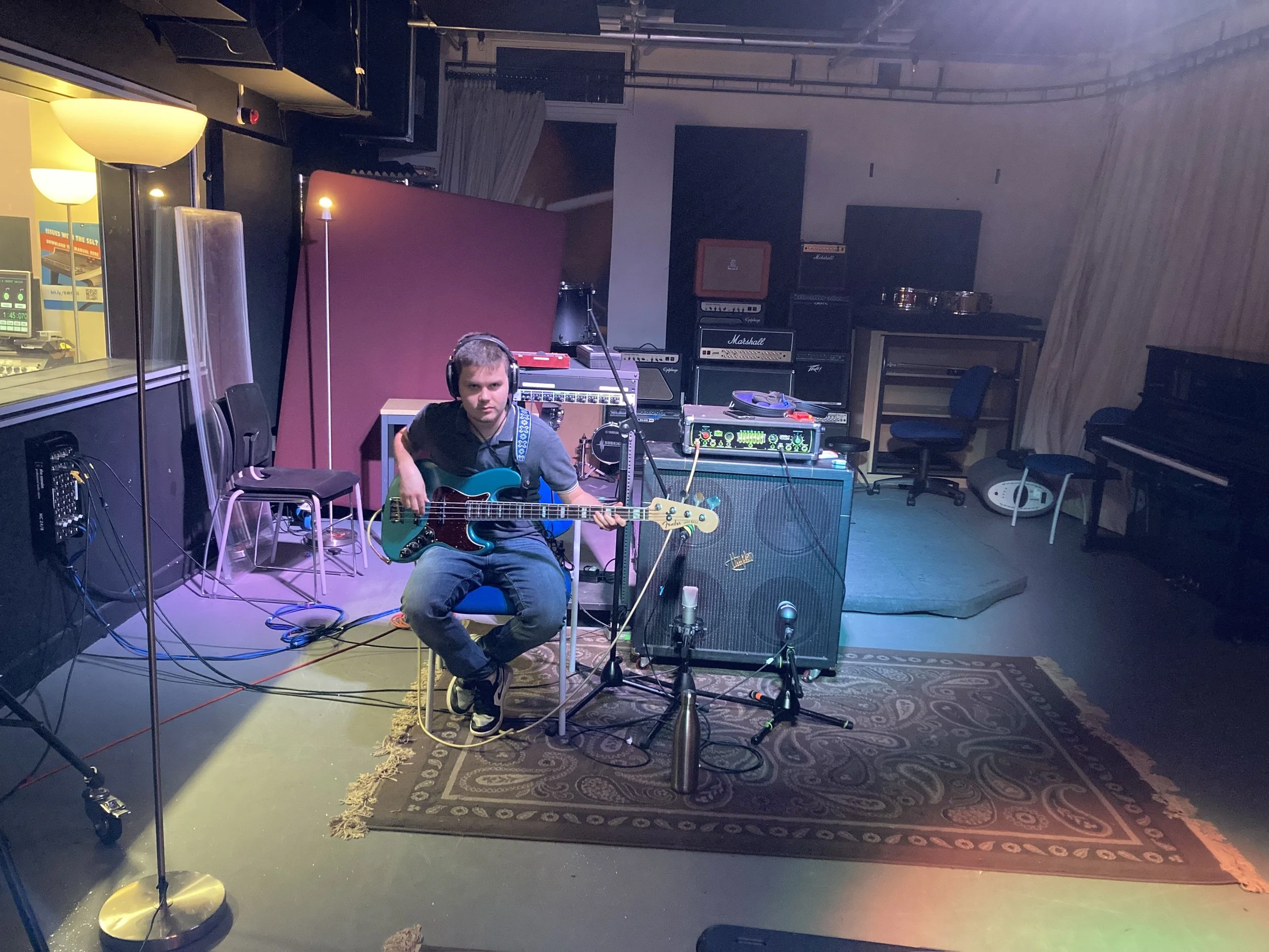 A young man with headphones sitting in front of music equipment and guitars in a music studio.