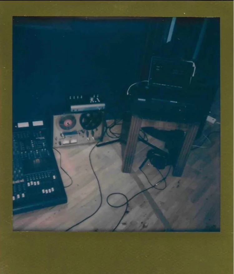 DJ equipment setup including a mixer, turntables, a laptop on a small table, and various cables on a wooden floor.