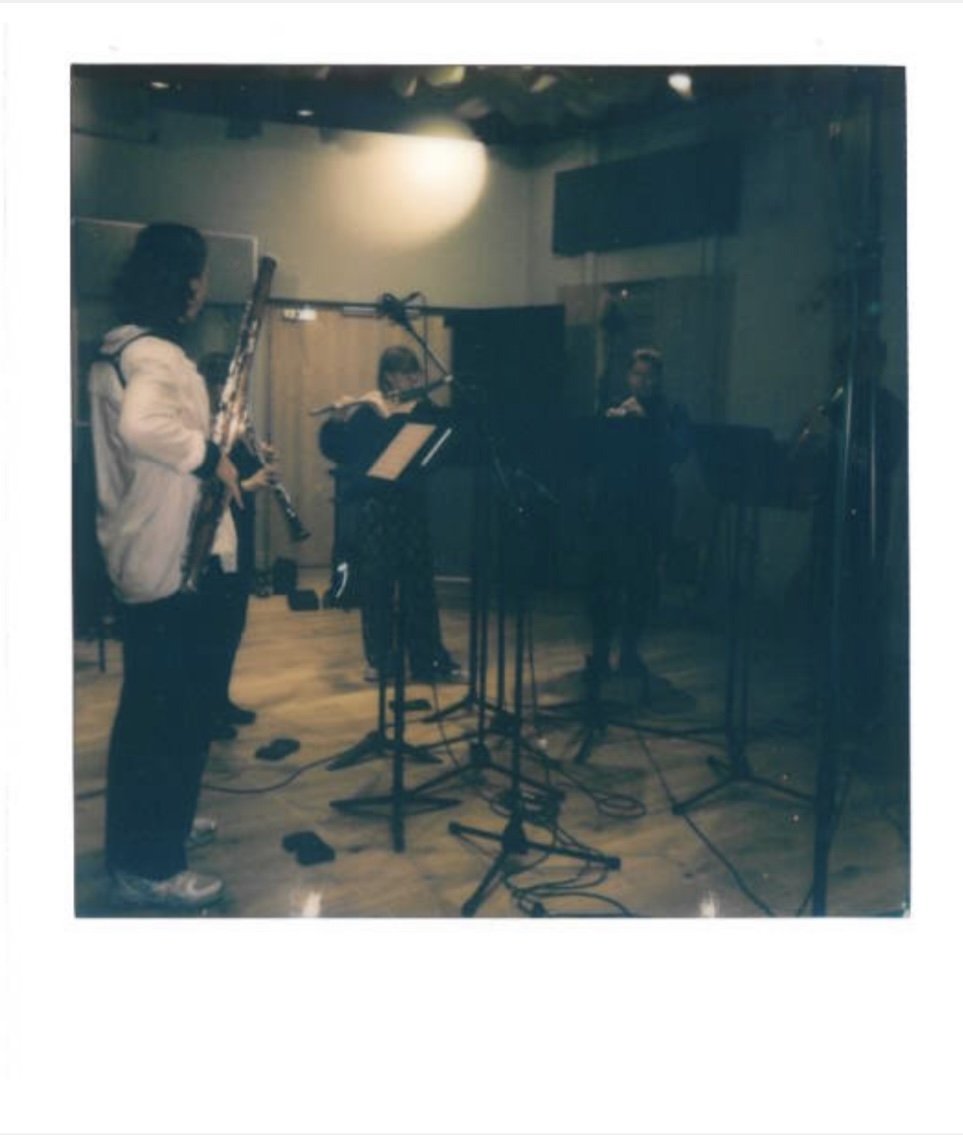Musicians practicing in a recording studio, with one playing a saxophone and others playing a keyboard and a guitar.