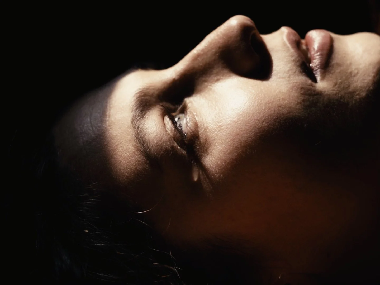 Close-up of a woman's face with closed eyes, lying down in low light.