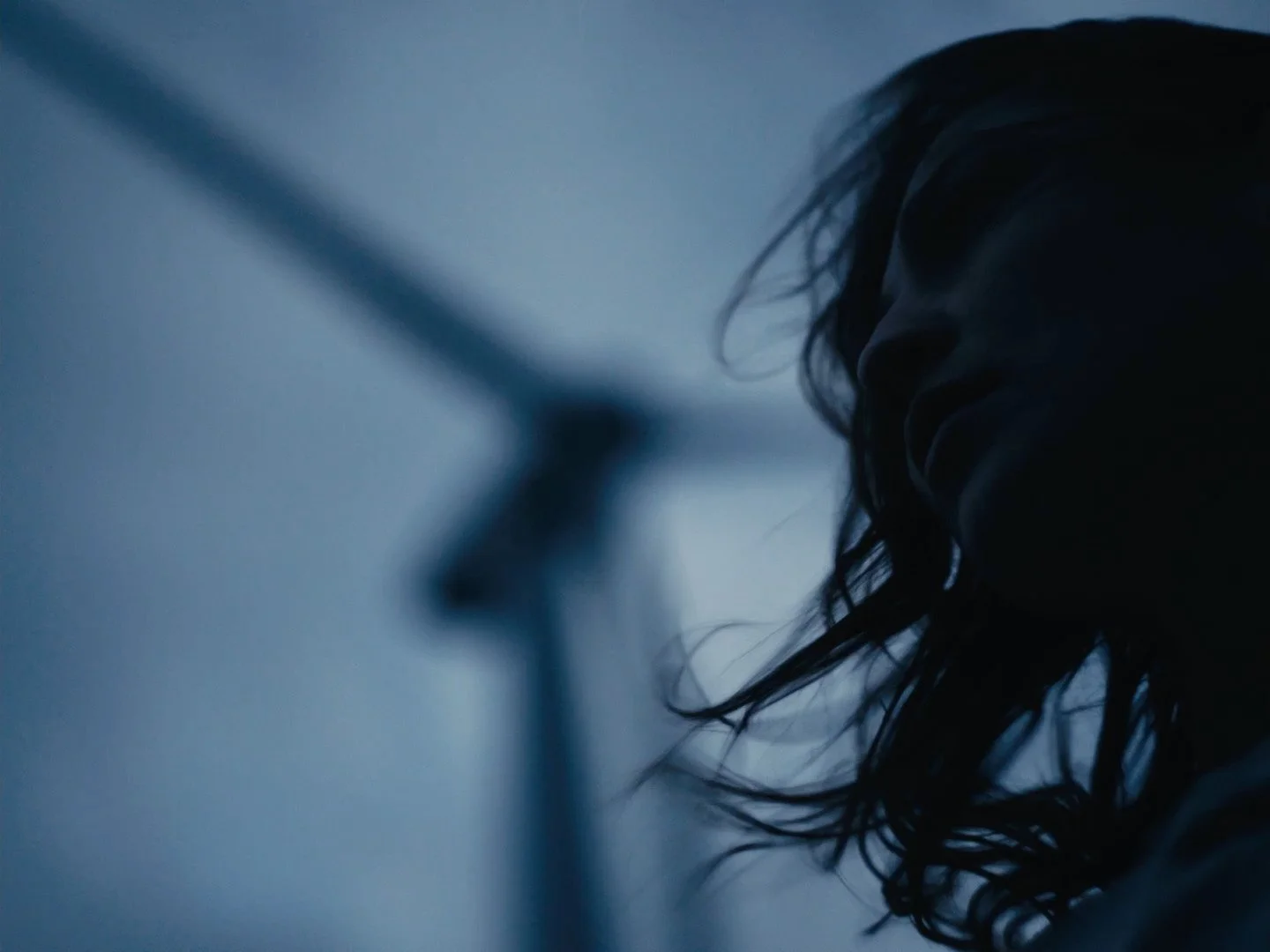 Silhouette of a woman with wet hair, smiling in a dimly lit room, with a blurred mirror in the background.